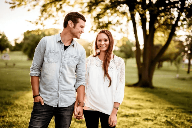 A young man and woman holding hands and smiling in a park during sunset.