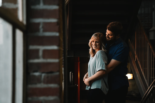A couple smiling and hugging on a staircase in a dimly lit urban setting.