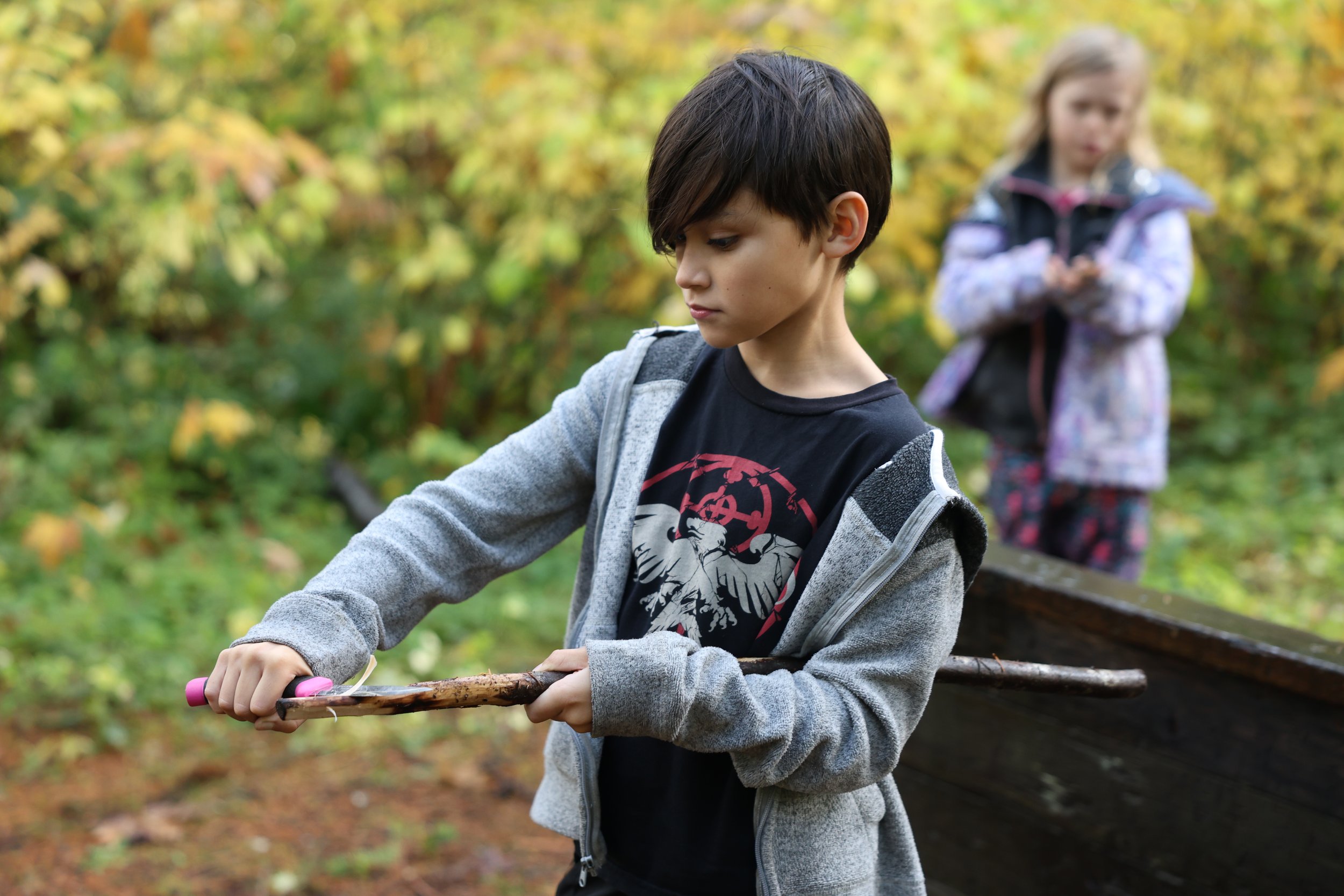 Elementary school student outside carving a stick at nonprofit independent private school, the Portland Forest School where academics and mental health are important. A community based nontraditional school for elementary and middle school students w