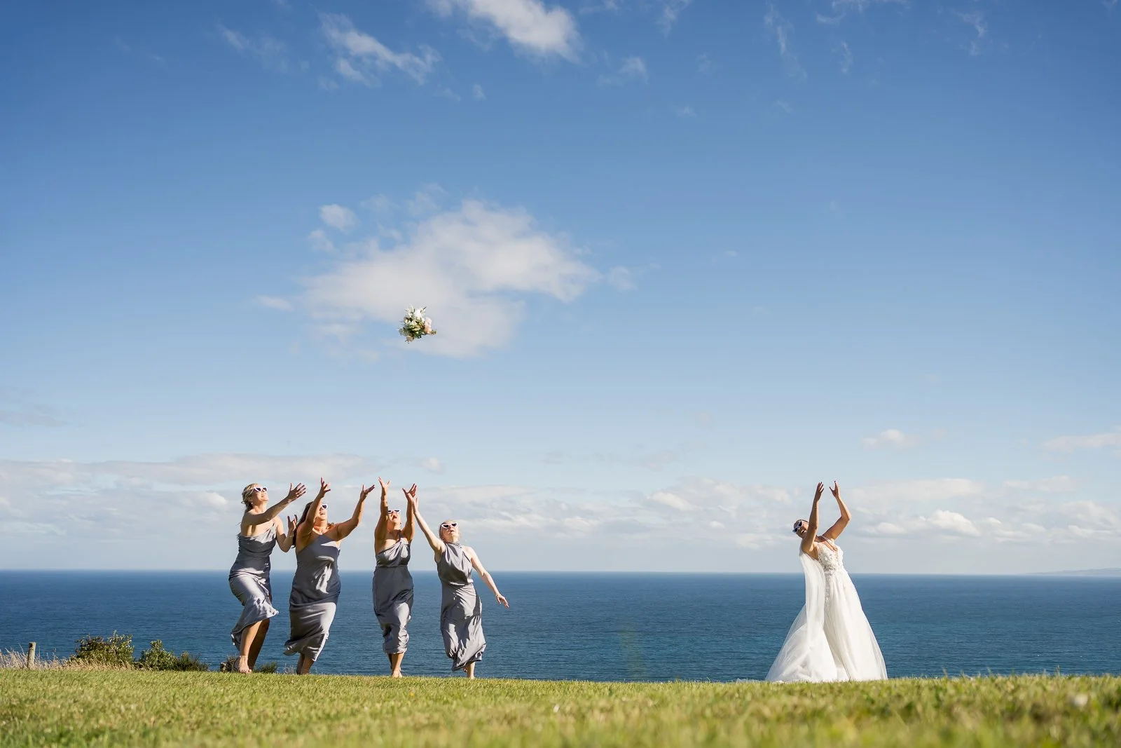 cinematic shot of bride tossing bouquet into the air for her bridesmaids to catch, stunning blue skies 