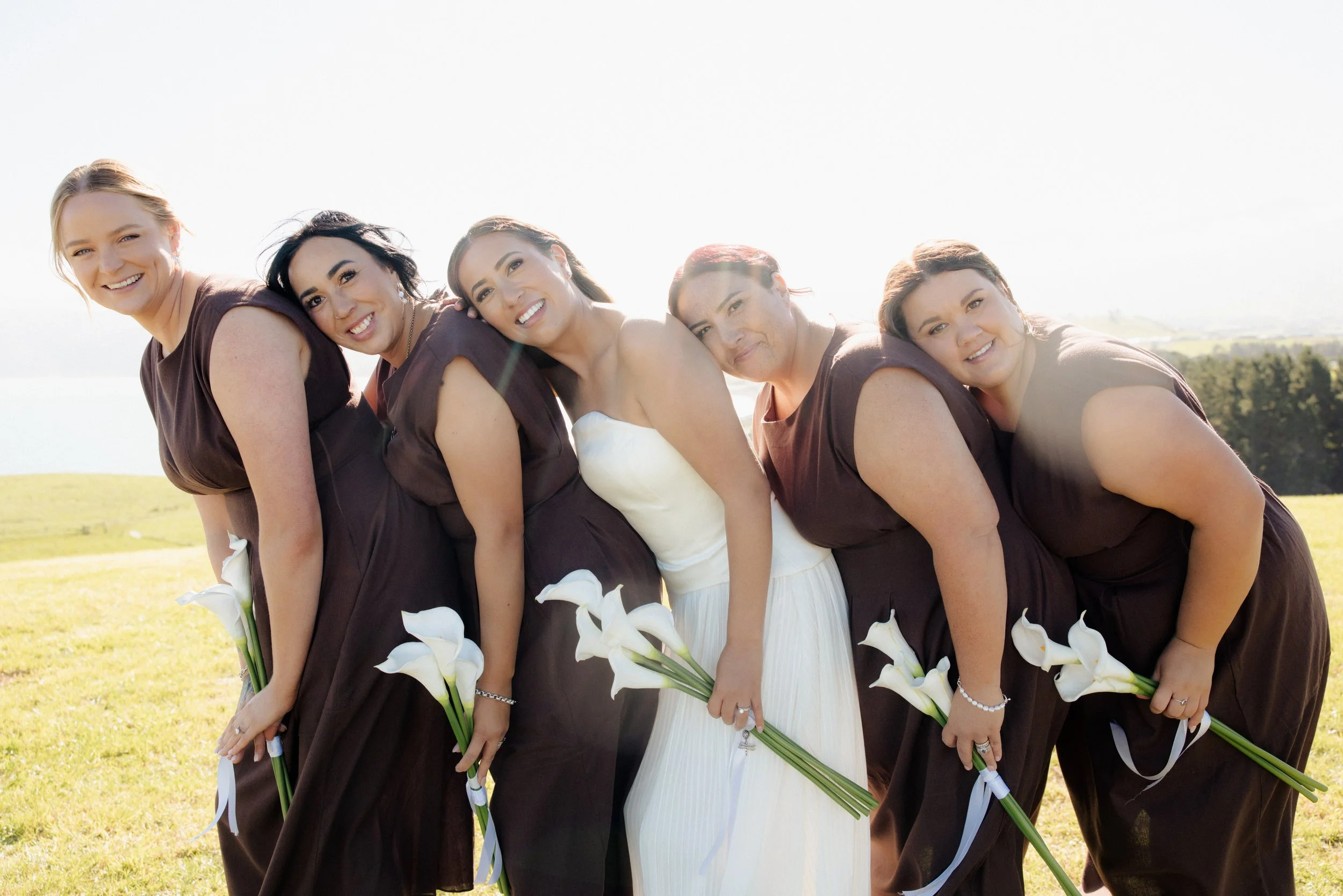 Bride and her bridesmaids wearing chocolate brown dresses holding their calla lily bouquets at golden hour