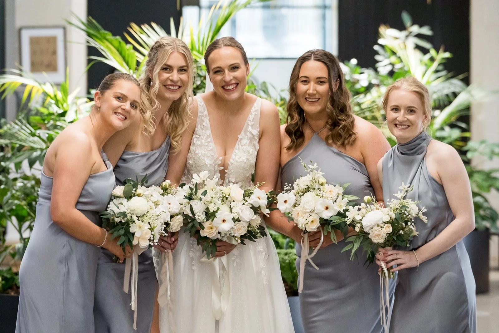 Bridesmaids wearing steel blue bridesmaid dresses and bride posing holding lush classic bouquets all artificial