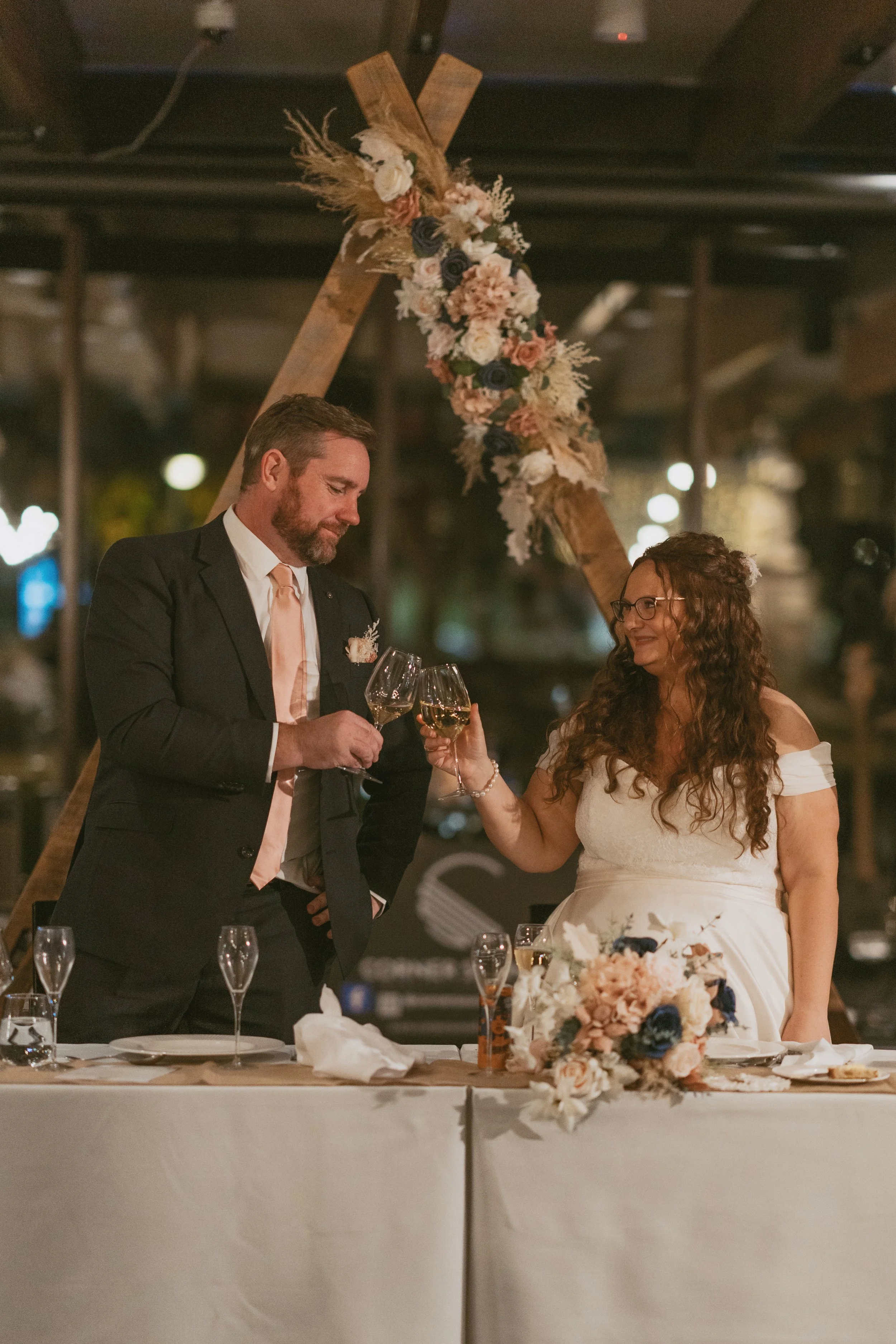 Bride and groom toasting at their reception with triangle arch with faux flowers behind them