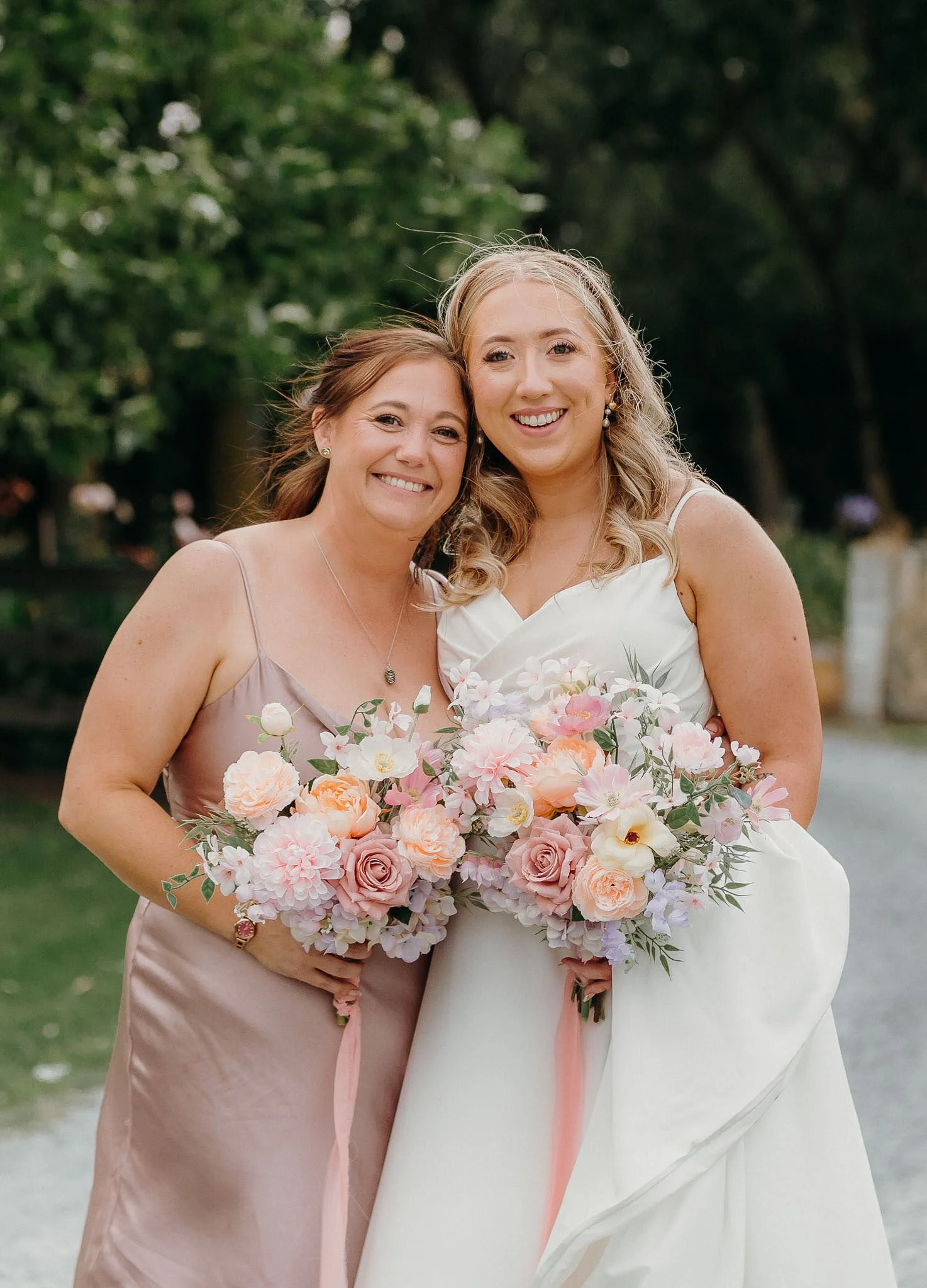 Bride and maid of honor posing for wedding photographer holding pastel bouquets