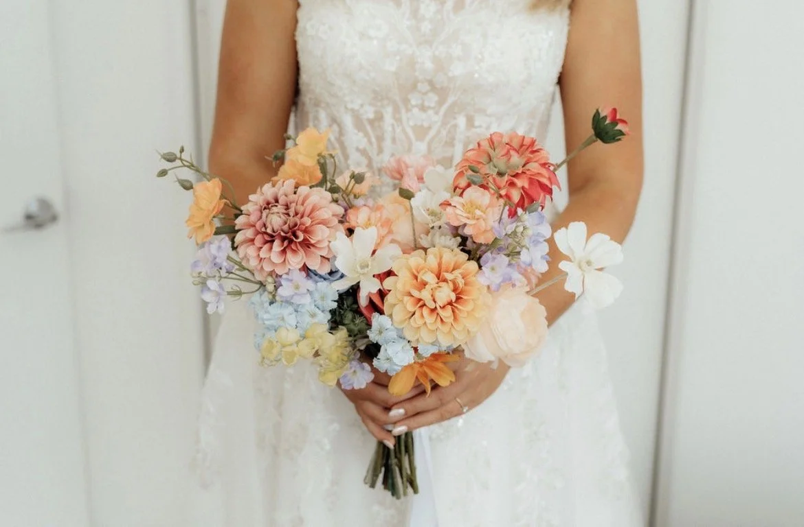 Person in a white wedding dress holding a bouquet of pastel-colored flowers.