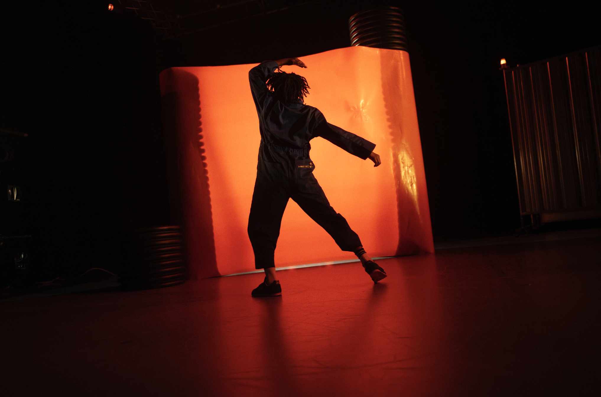 A boy dancing in front of a large, illuminated orange backdrop in a dark room.