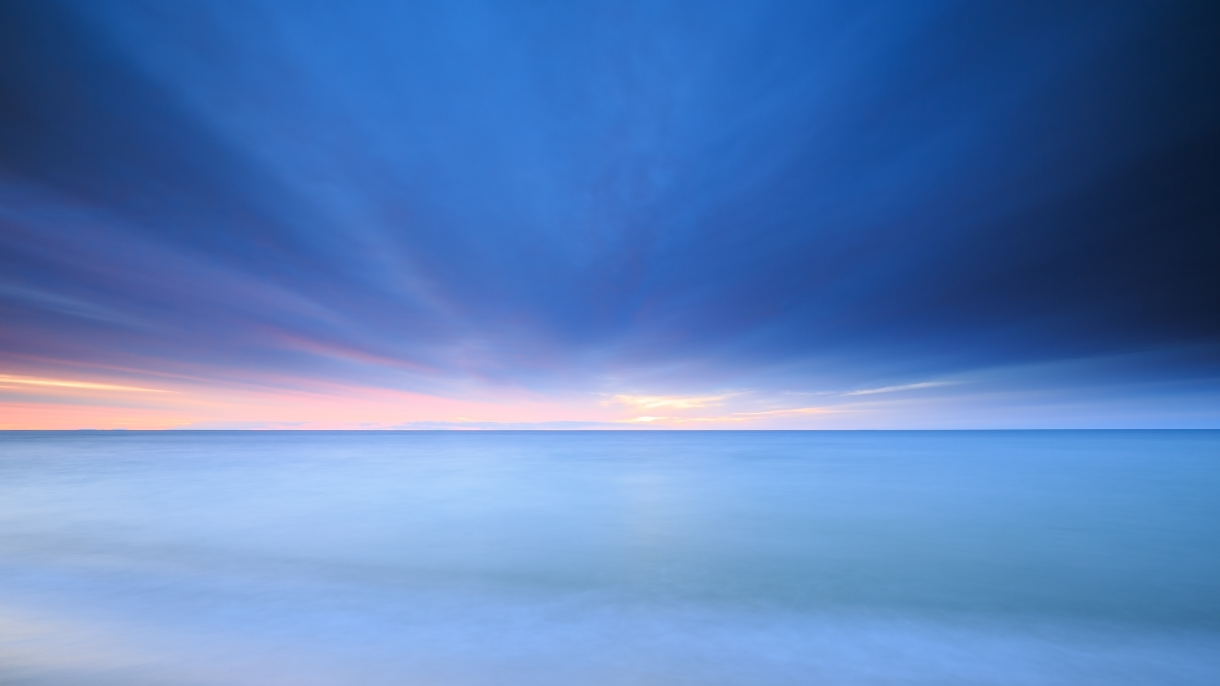 A calm ocean under a cloudy sky during sunset with soft colors.