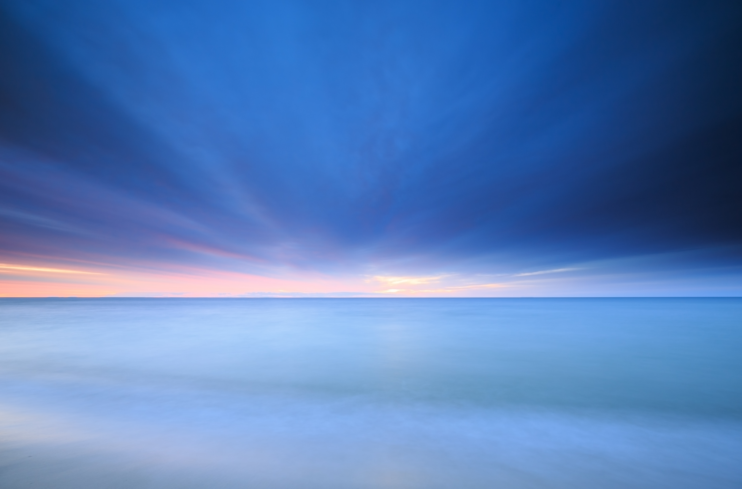 A serene seascape with a smooth horizon, calm blue water, and a sky with dark clouds and a subtle hint of sunset colors.