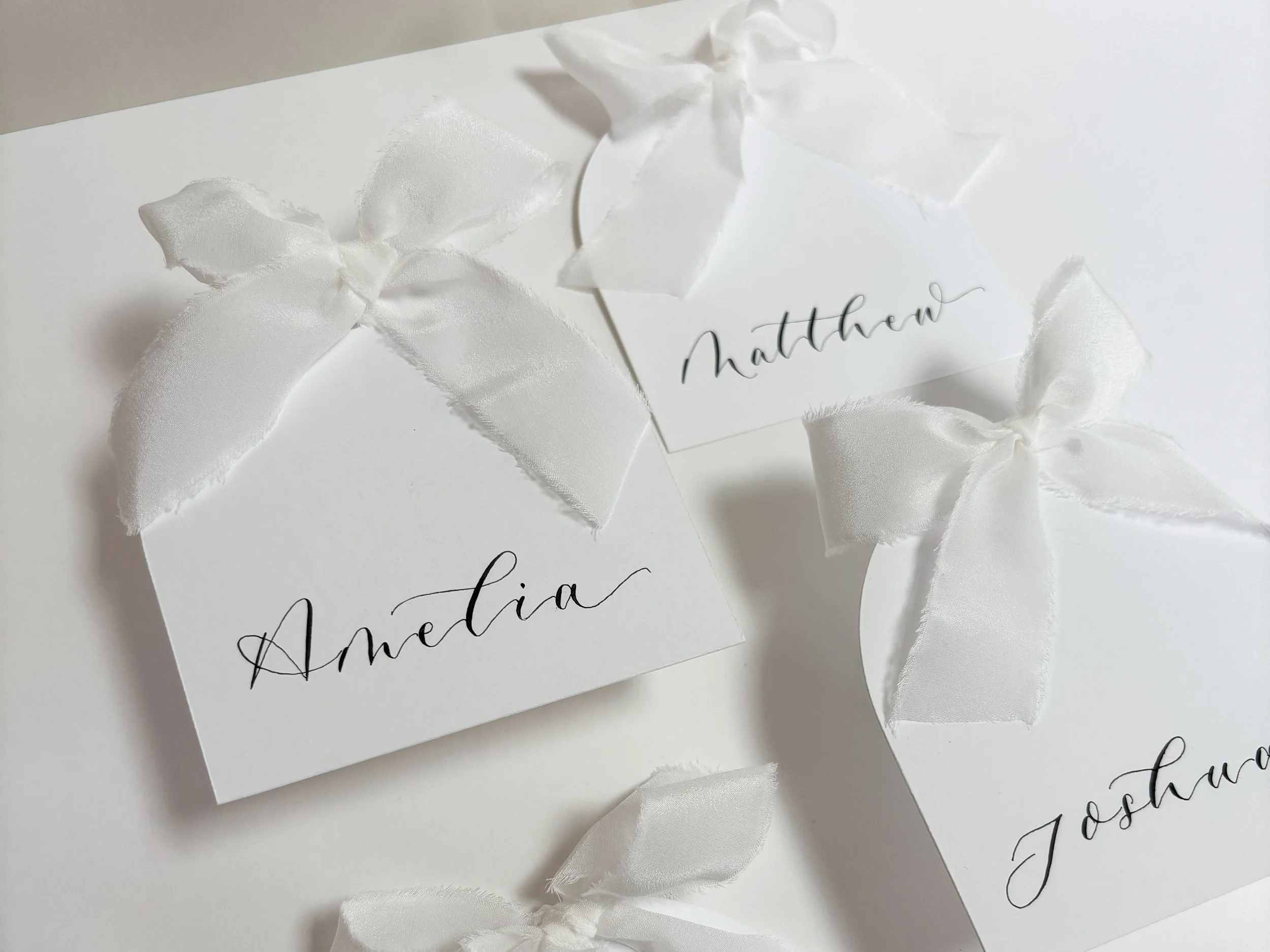 Elegant Arched white place cards finished with handwritten modern calligraphy and white silk ribbon