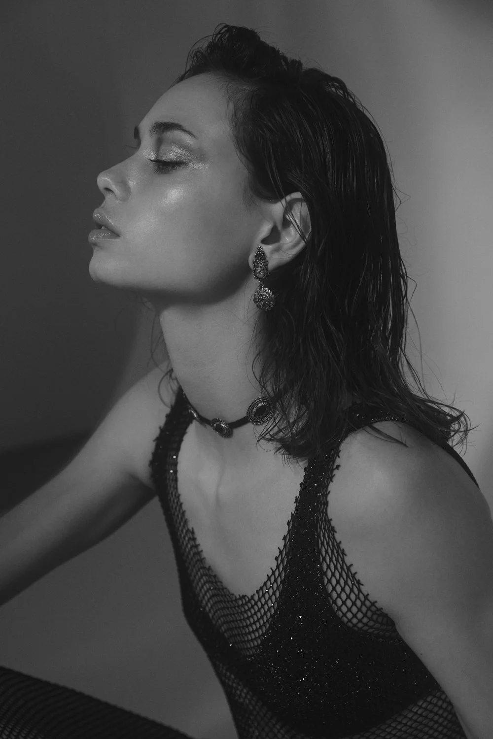 A black and white portrait of a woman with wet hair wearing Vintage jewelry, Oseree swimwear and a sparkly fishnet dress by Zara.