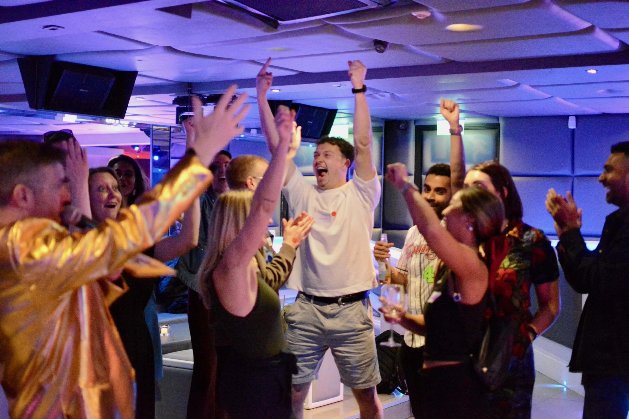 People enjoying a lively celebration or party in a nightclub or bar, with some raising their hands and smiling.