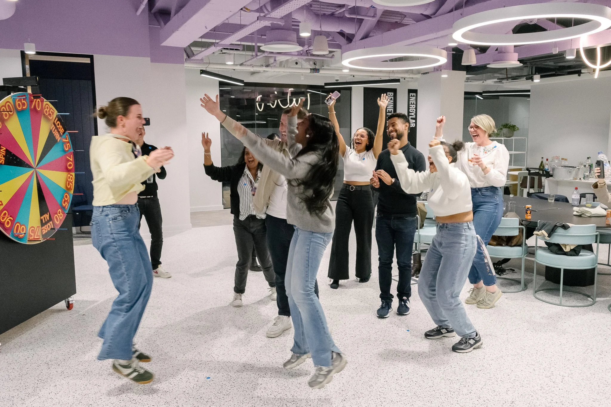 Group of people joyfully dancing and celebrating in an indoor space with modern lighting and decor.