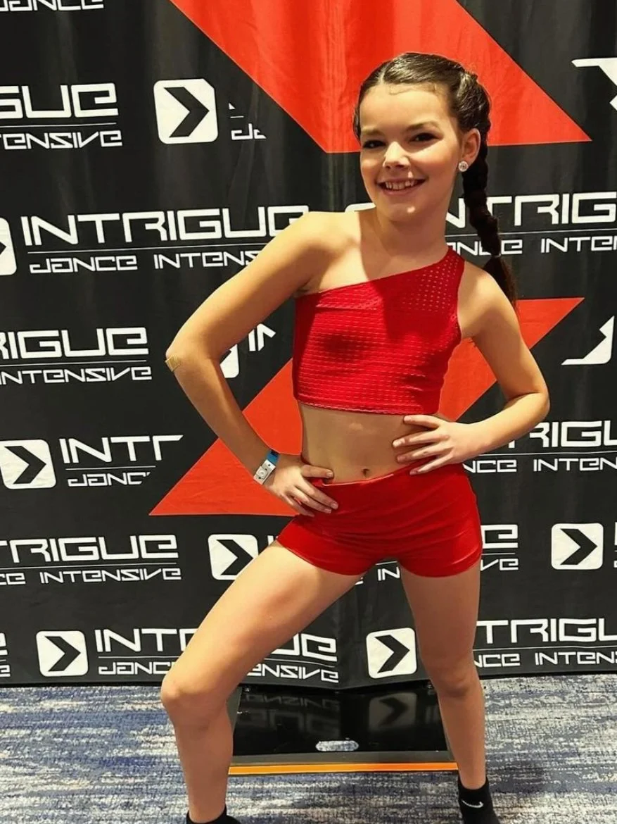 Confident dancer in a bold red one-shoulder Tilly Blue set, posing backstage at Intrigue Dance Intensive—stylish, sleek, and competition-ready.