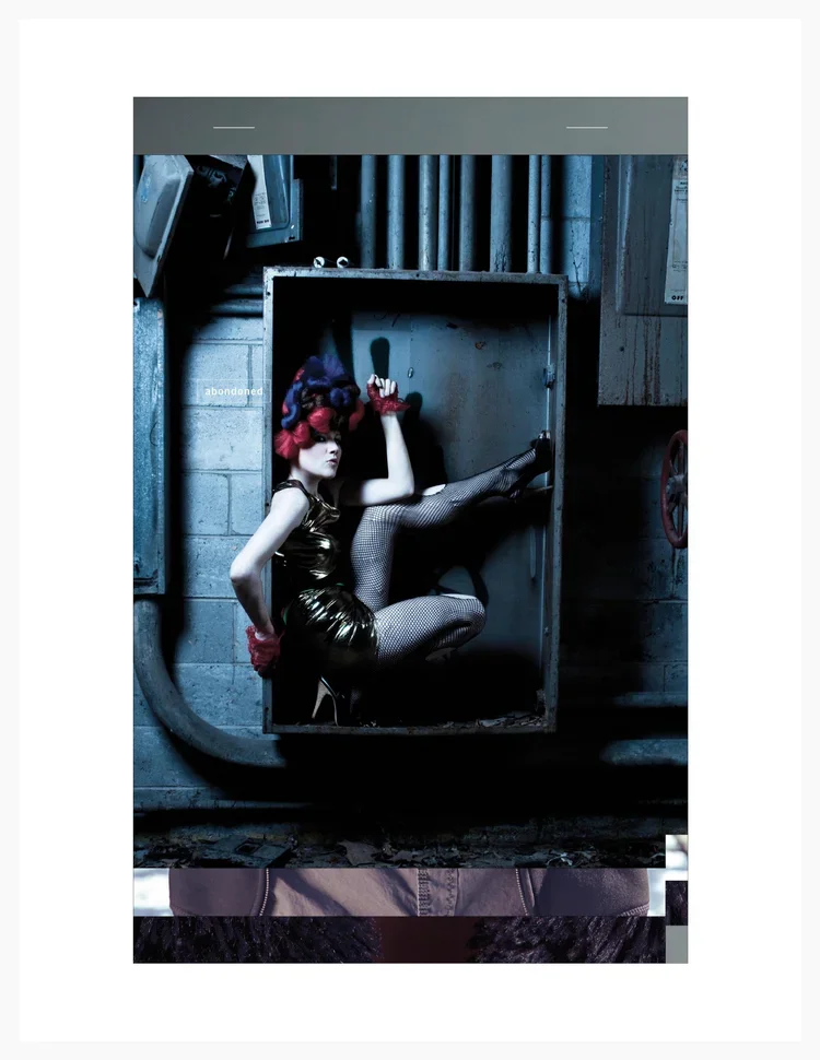 A woman with colorful hair, wearing a shiny gold dress, fishnet stockings, and red gloves, sitting inside an open electrical box in an industrial setting with pipes and a concrete wall.
