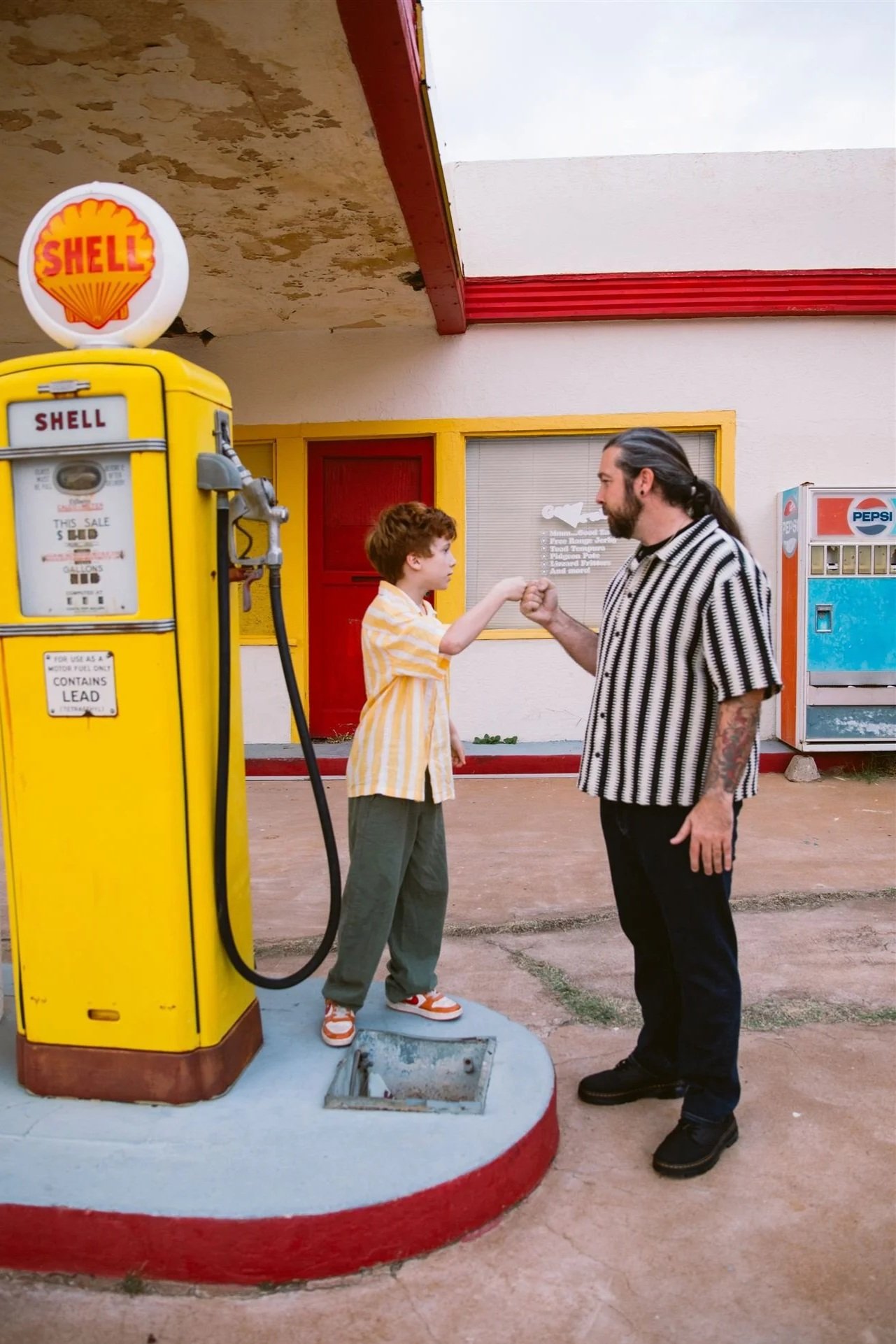 A father and son candidly posing next to a vintage Shell gas station pump during a cinematic family photography session in the historic neighborhood of Lowell in Bisbee, Arizona