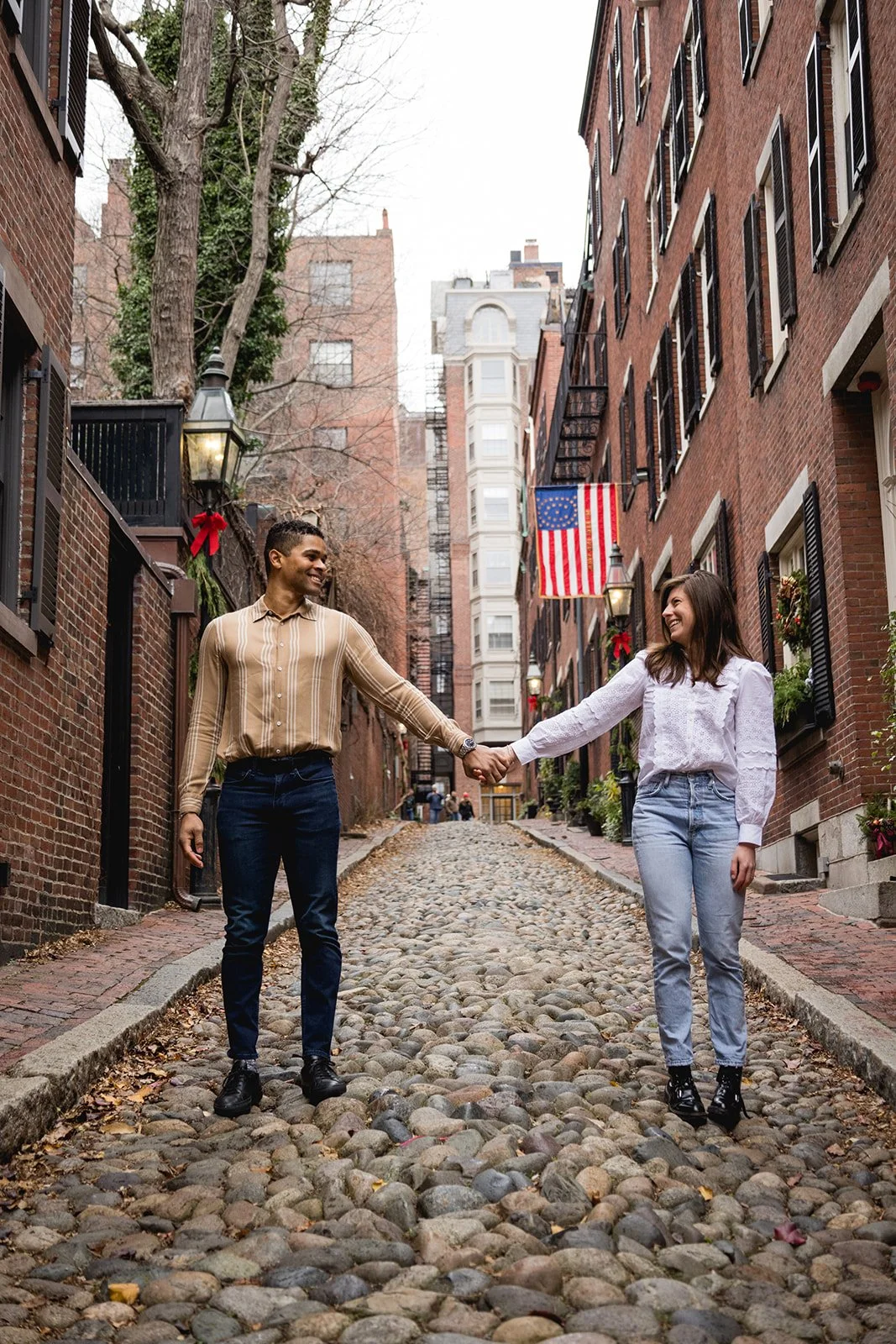 Couple holding hands while walking down a cobblestone street in Beacon Hill during a Boston engagement session.