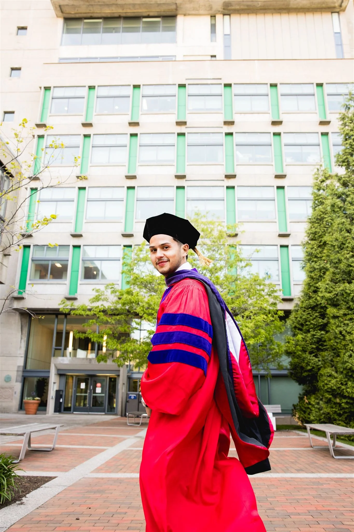 Graduate student in doctoral robes posing on a modern campus courtyard during a graduation photography session in Boston