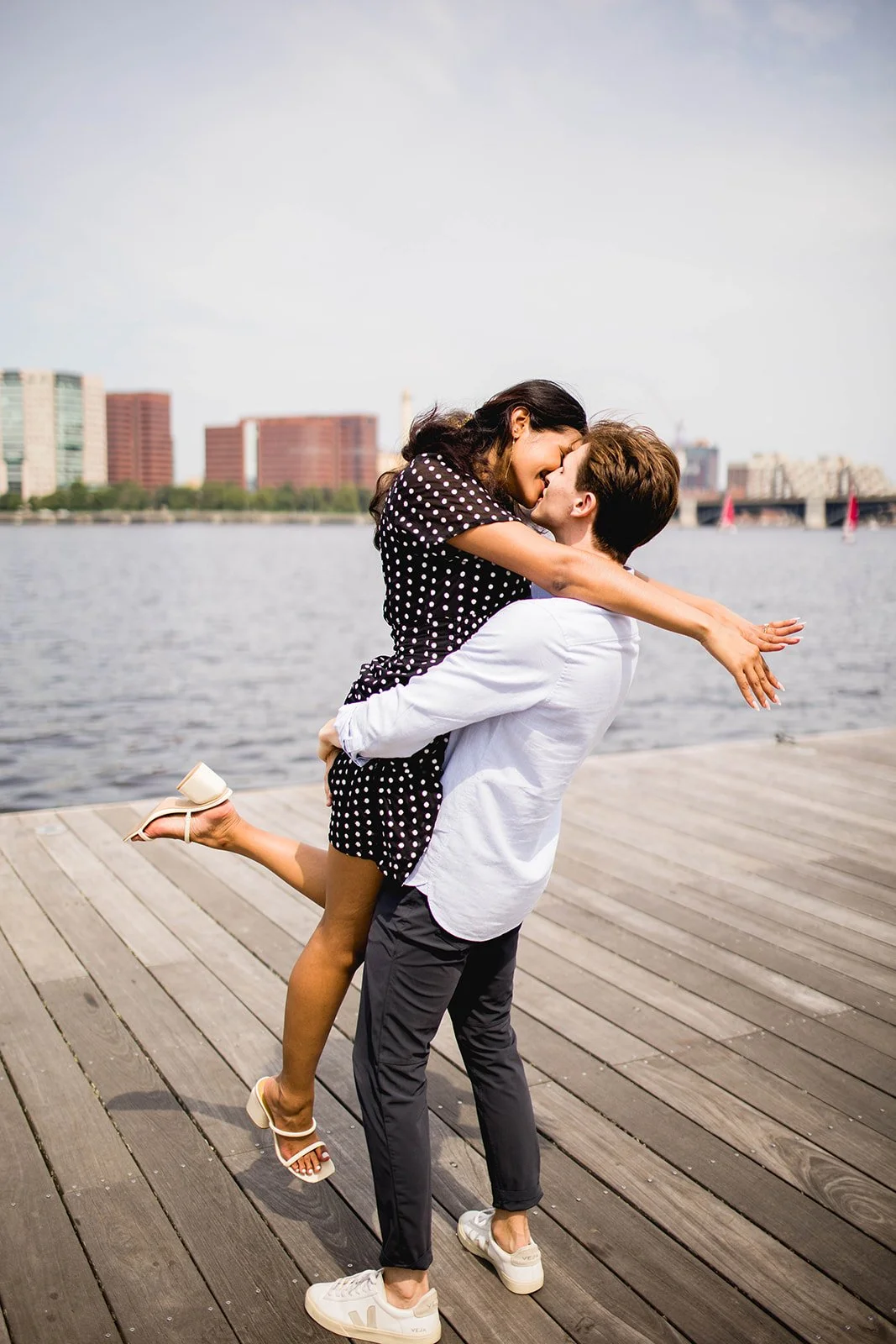Couple celebrating together on the waterfront at the Seaport District with the Boston skyline behind them during an engagement photo session.