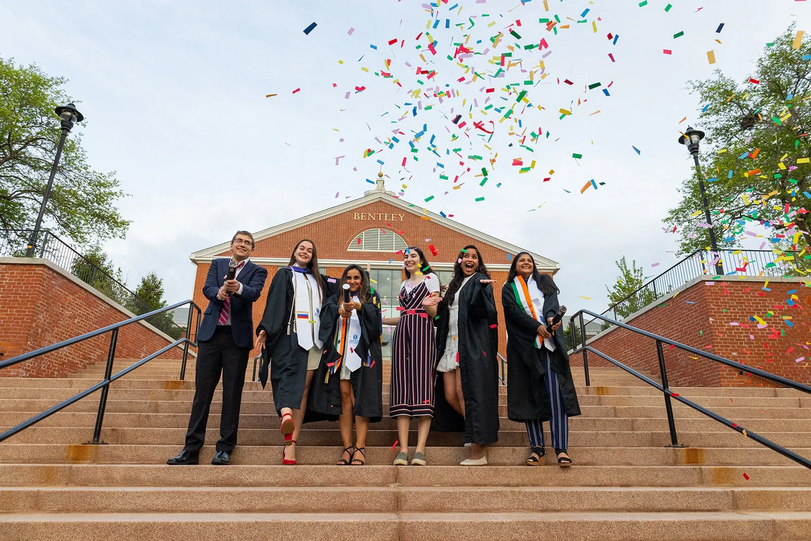 Group of graduates celebrating with confetti on the steps at Bentley University during a graduation photography session near Boston