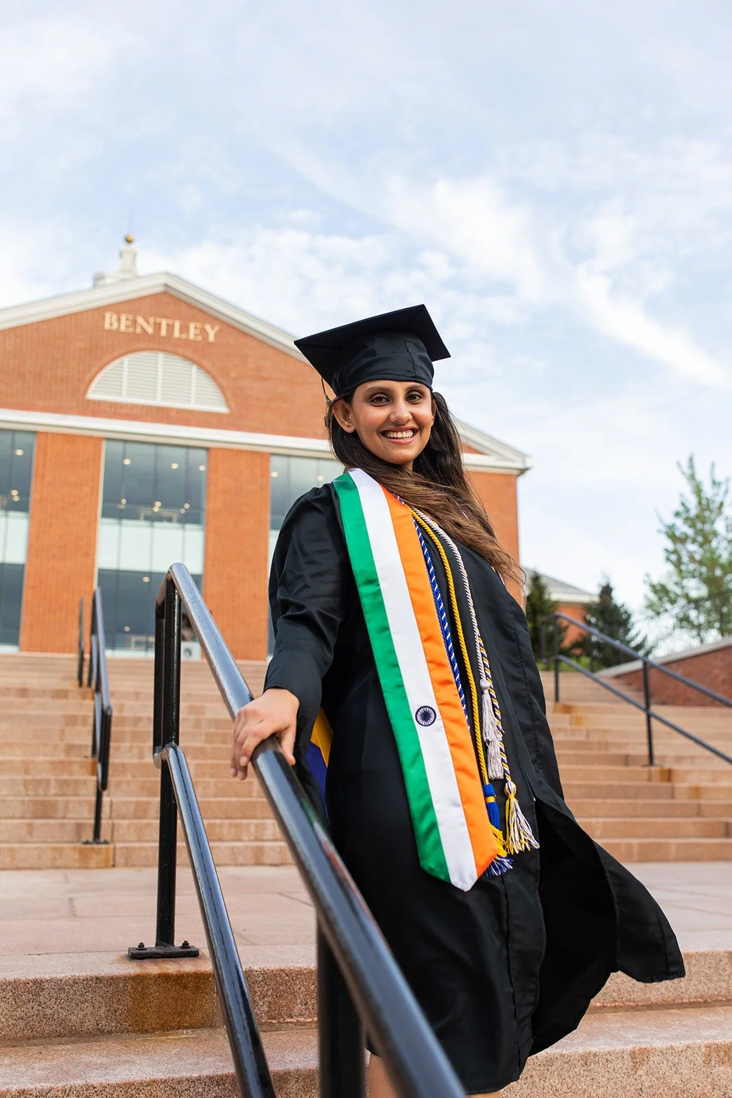 Senior graduate posing on the steps at Bentley University during a graduation photography session near Boston