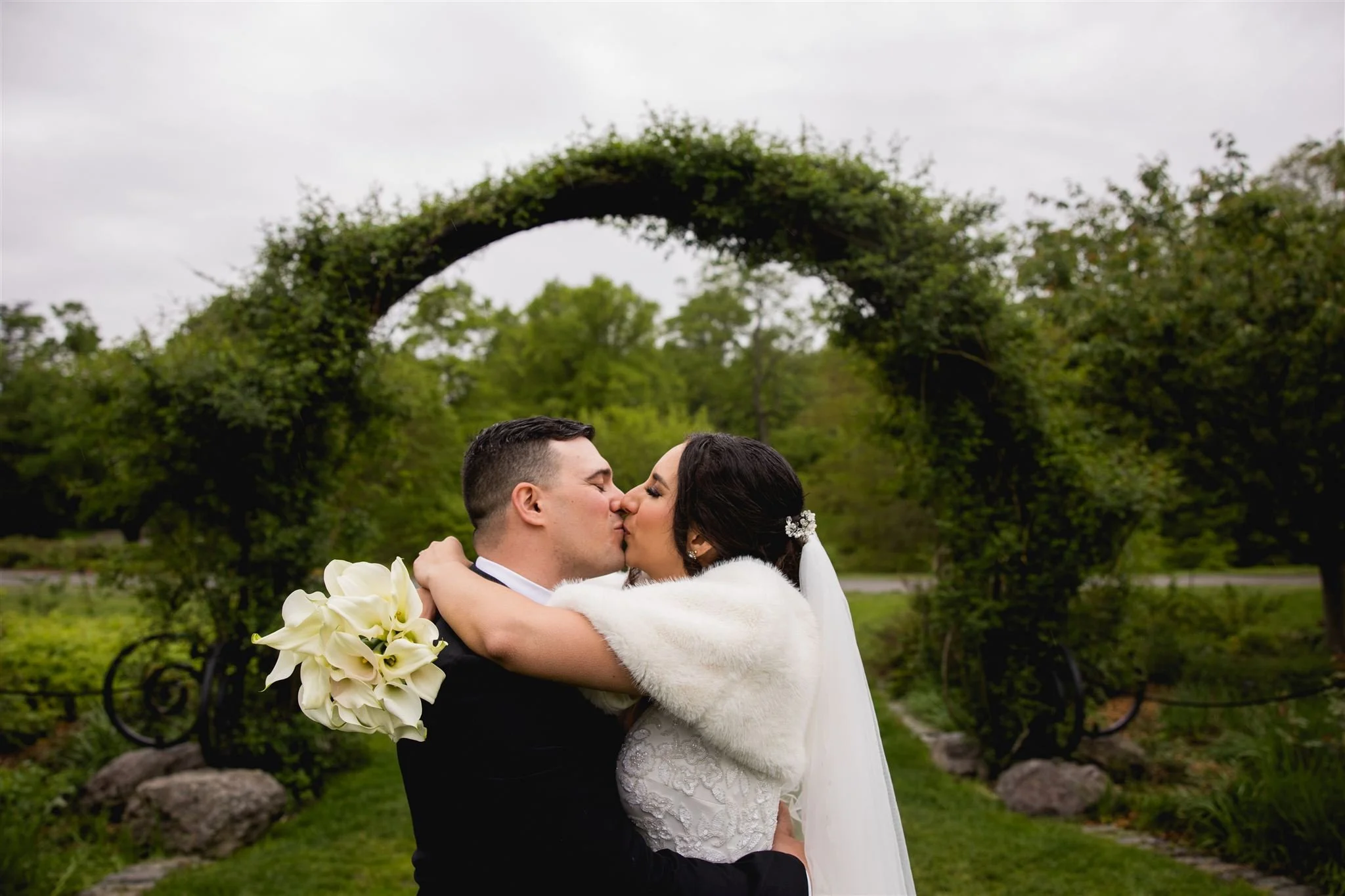 bride and groom share a kiss underneath a vine-lined archway at Arnold's Arboretum in Jamaica Plains Boston