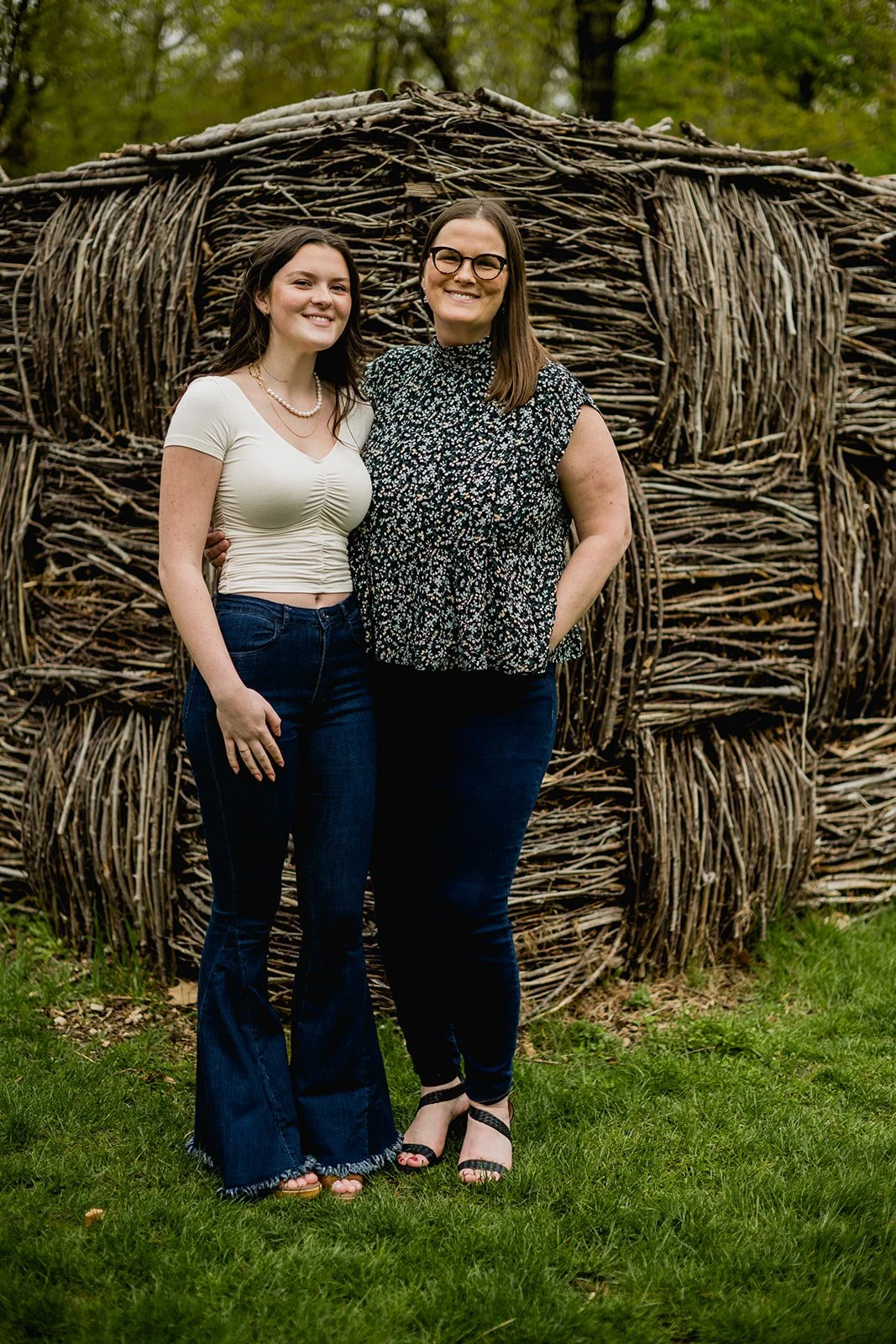 High school senior standing with her mother in front of a woven wooden sculpture during an outdoor photo session in Massachusetts.