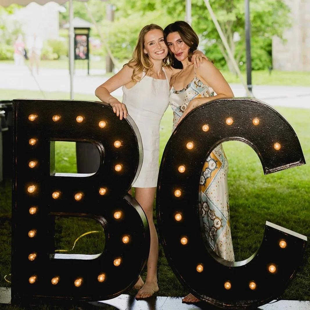 Boston College graduates posing together behind a large BC sign