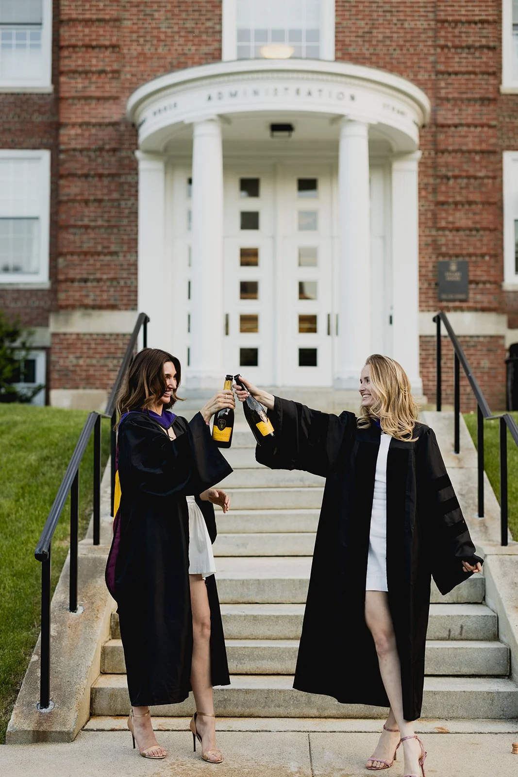 Boston College graduates celebrating in their cap and gown and drinking champagne in front of an iconic Boston College building