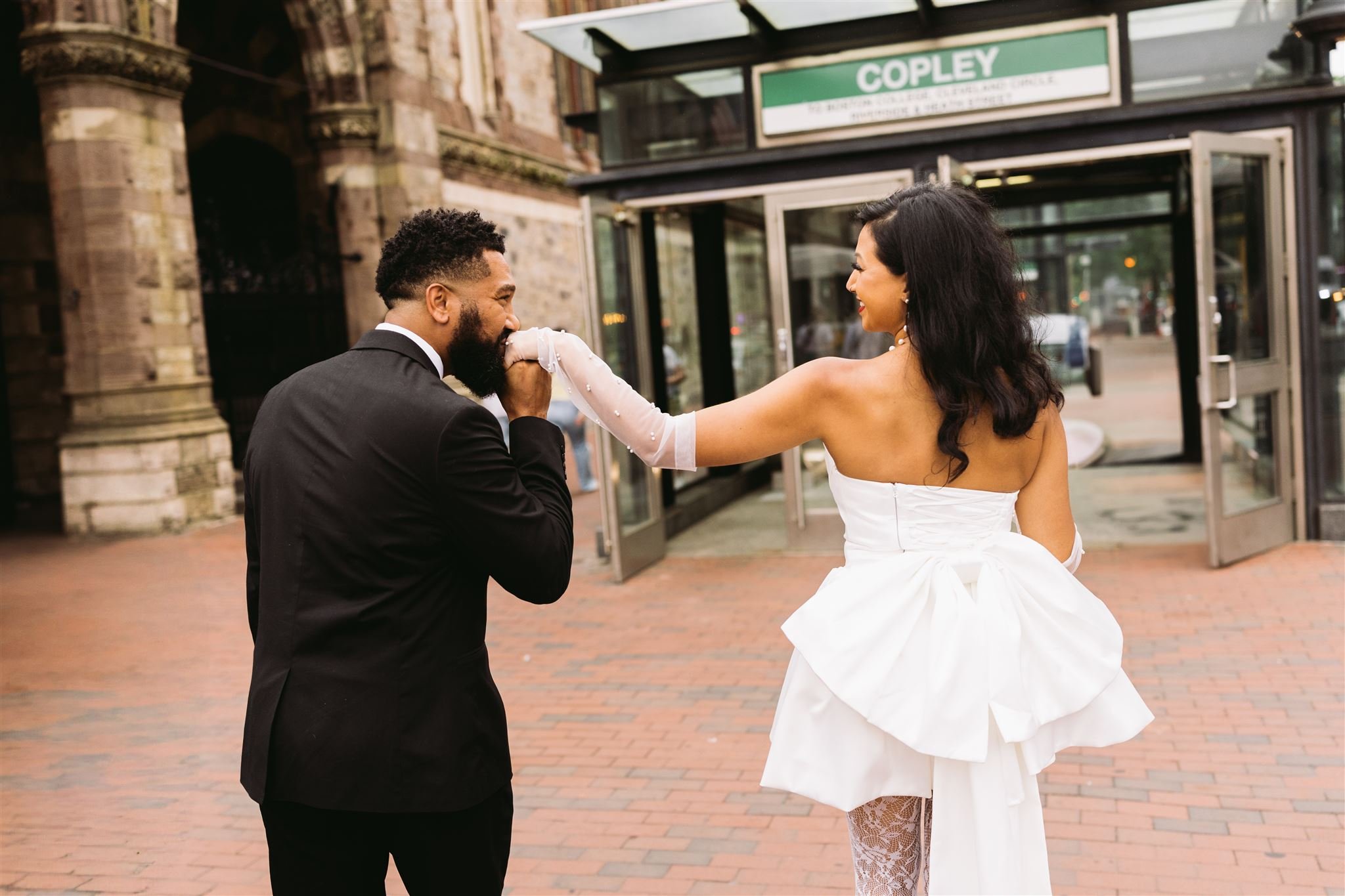 Boston engagement photos at Copley Square near Old South Church with couple walking and groom kissing bride’s hand
