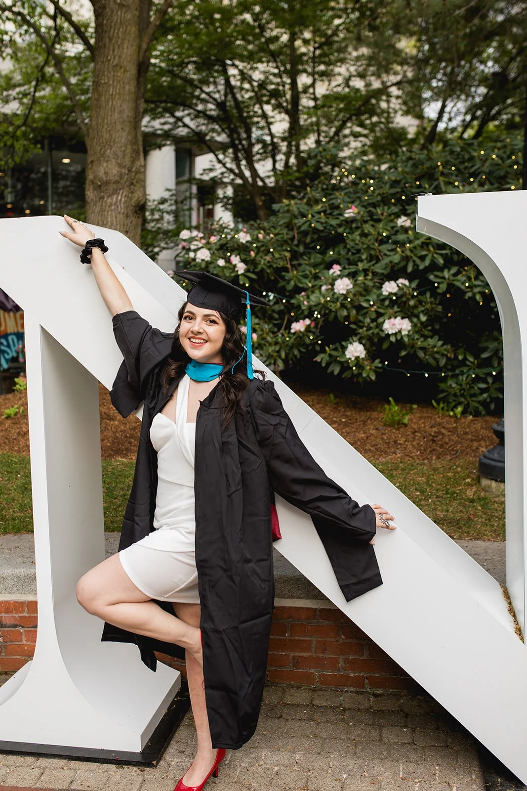 Senior graduate posing on a modern campus sculpture during a graduation photography session in Boston