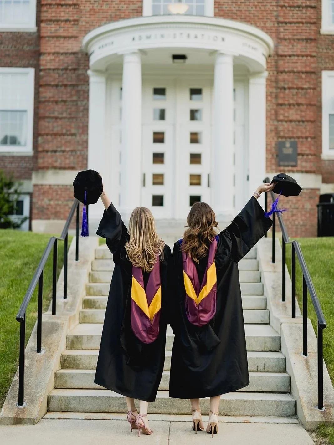 Boston College graduates in cap and gown holding their caps in the air in celebration.