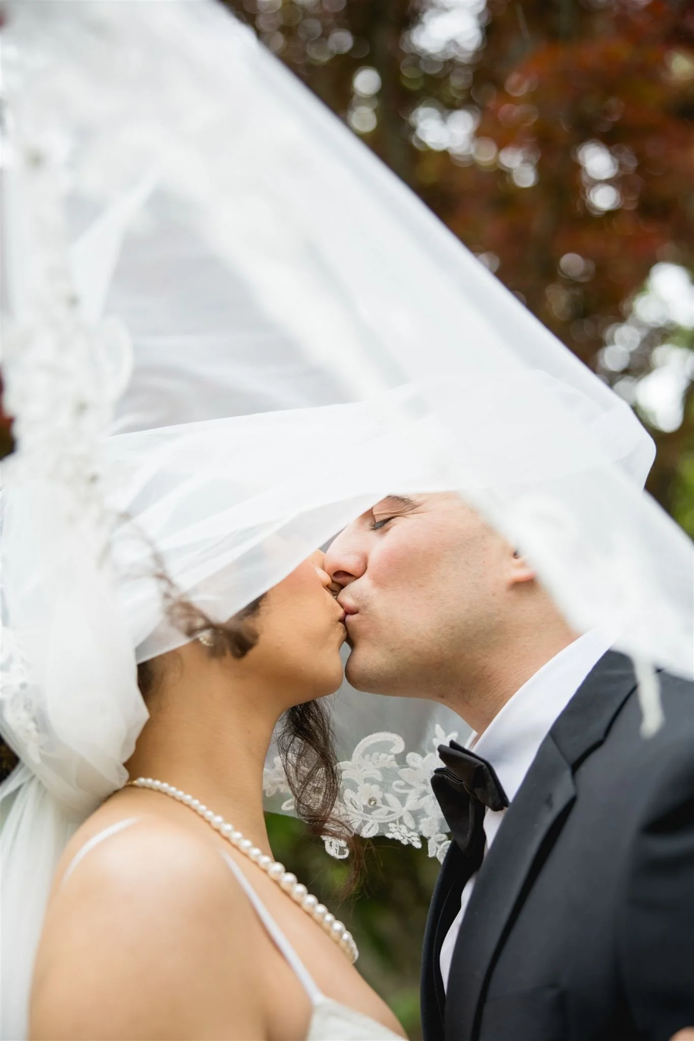 newly wed couple kissing under the bride's wedding veil in a outdoor micro wedding Boston setting