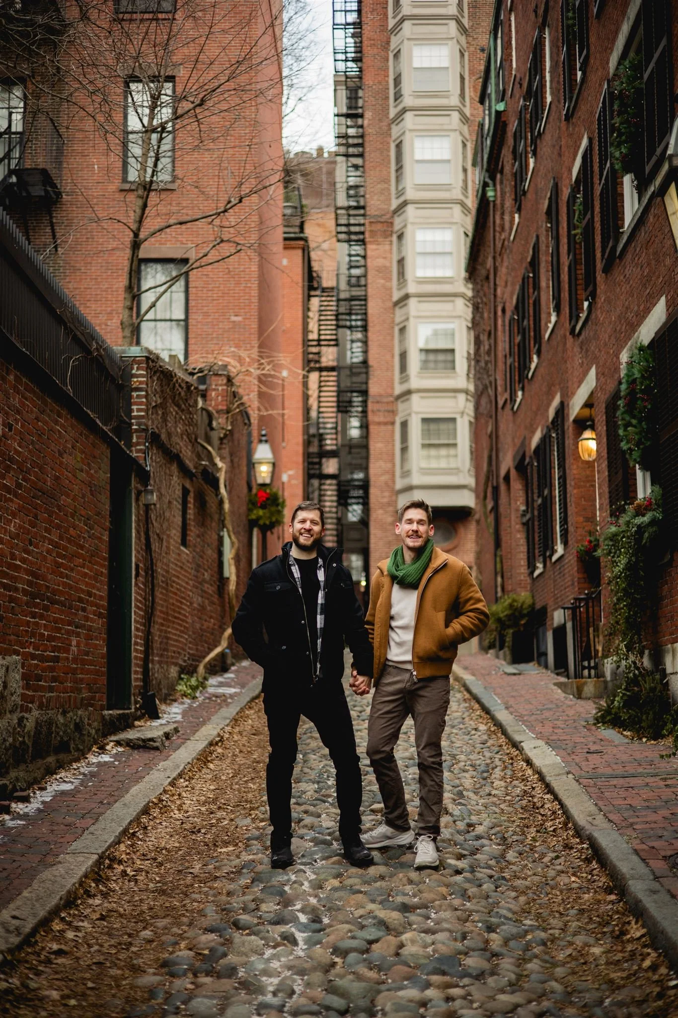 Engaged couple holding hands walking down a  cobblestone alley in Beacon Hill, Boston