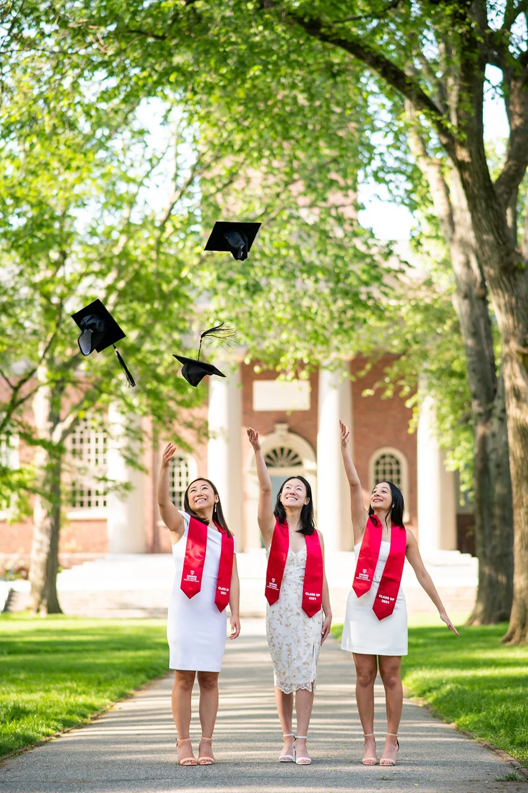 Three graduates tossing their caps at Harvard Yard during a graduation photography session in Boston