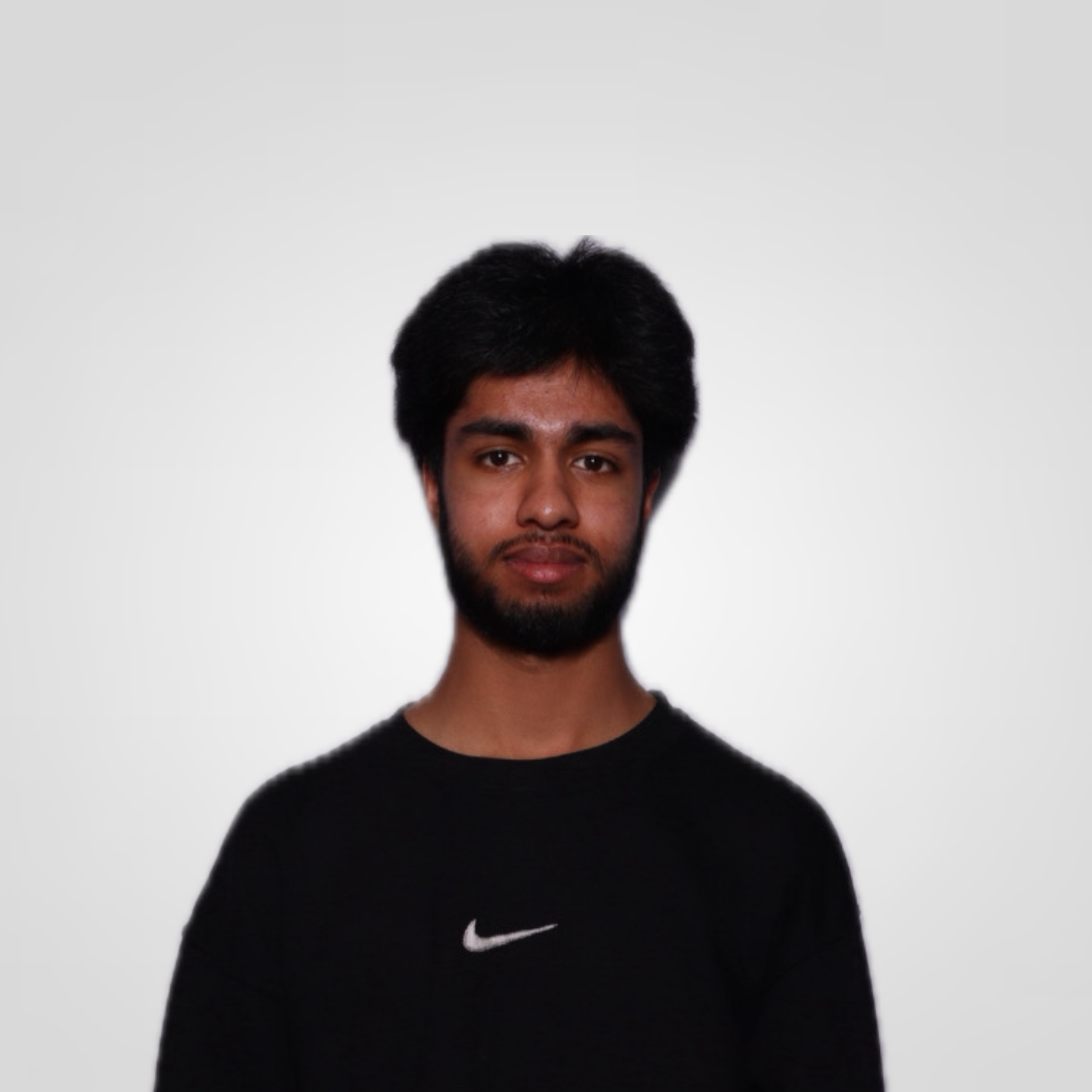 Portrait of a young man with dark hair and beard wearing a black Nike shirt, facing forward against a plain light background.