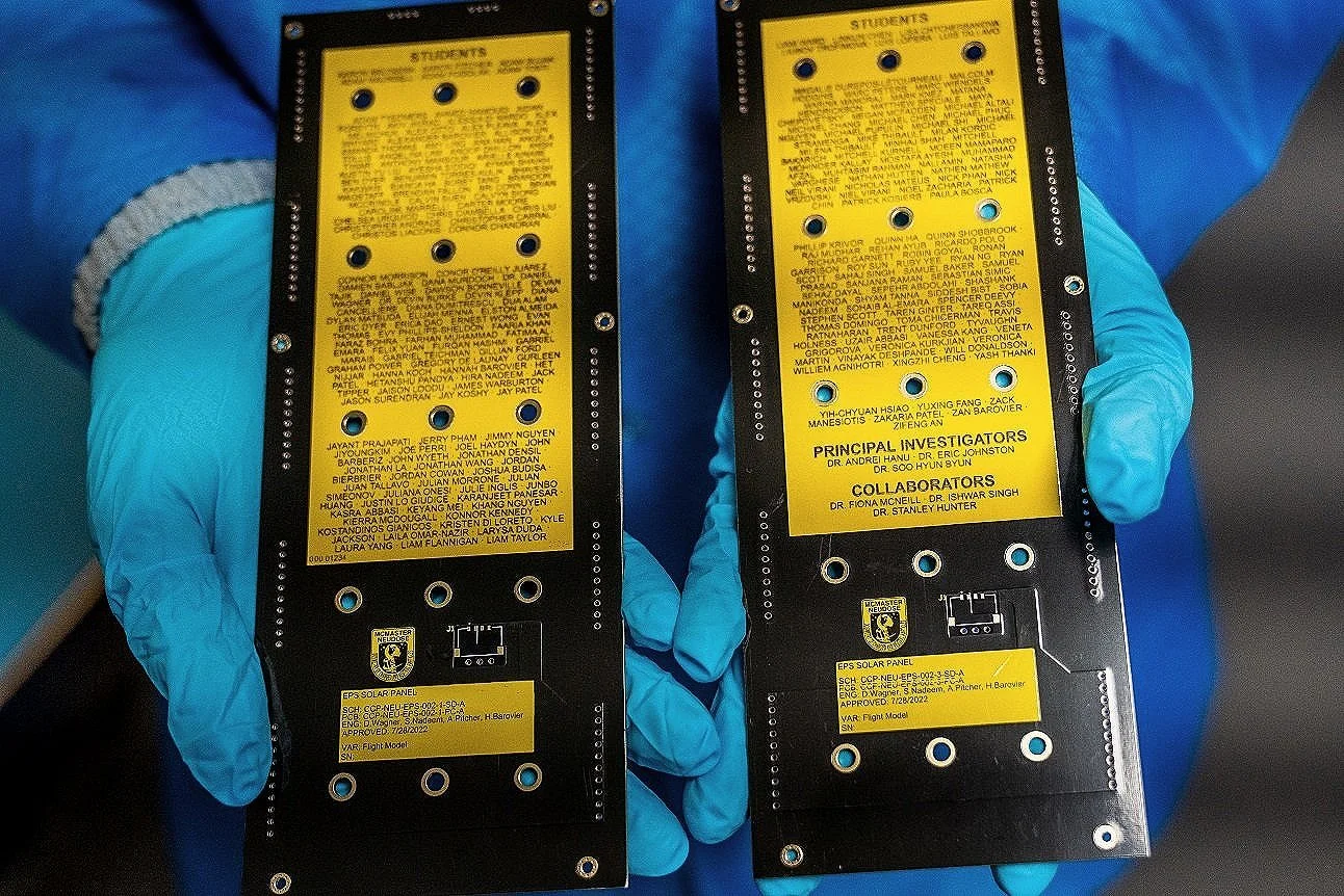 Two black rectangular solar panels with yellow labels held by gloved hands.