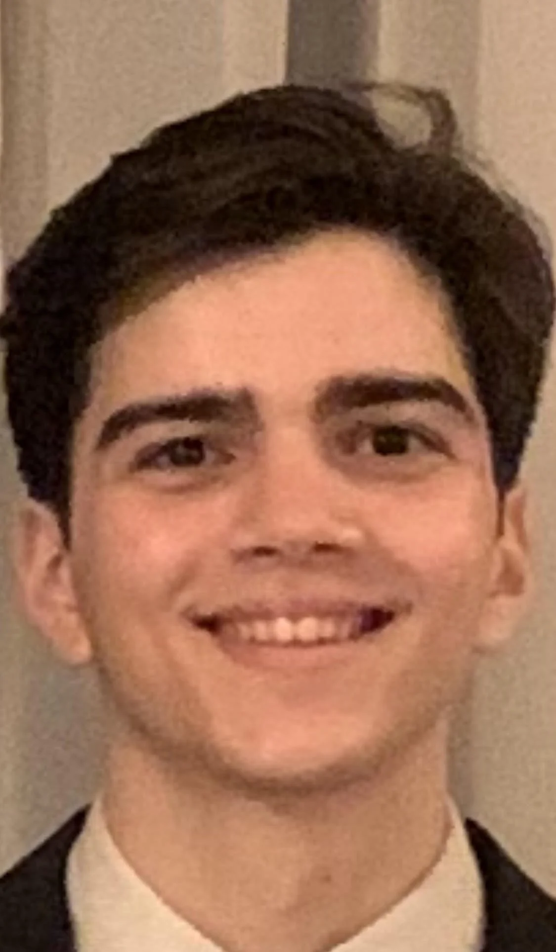 A young man with dark hair styled to the side, smiling, wearing a tuxedo with a white shirt and black bow tie.