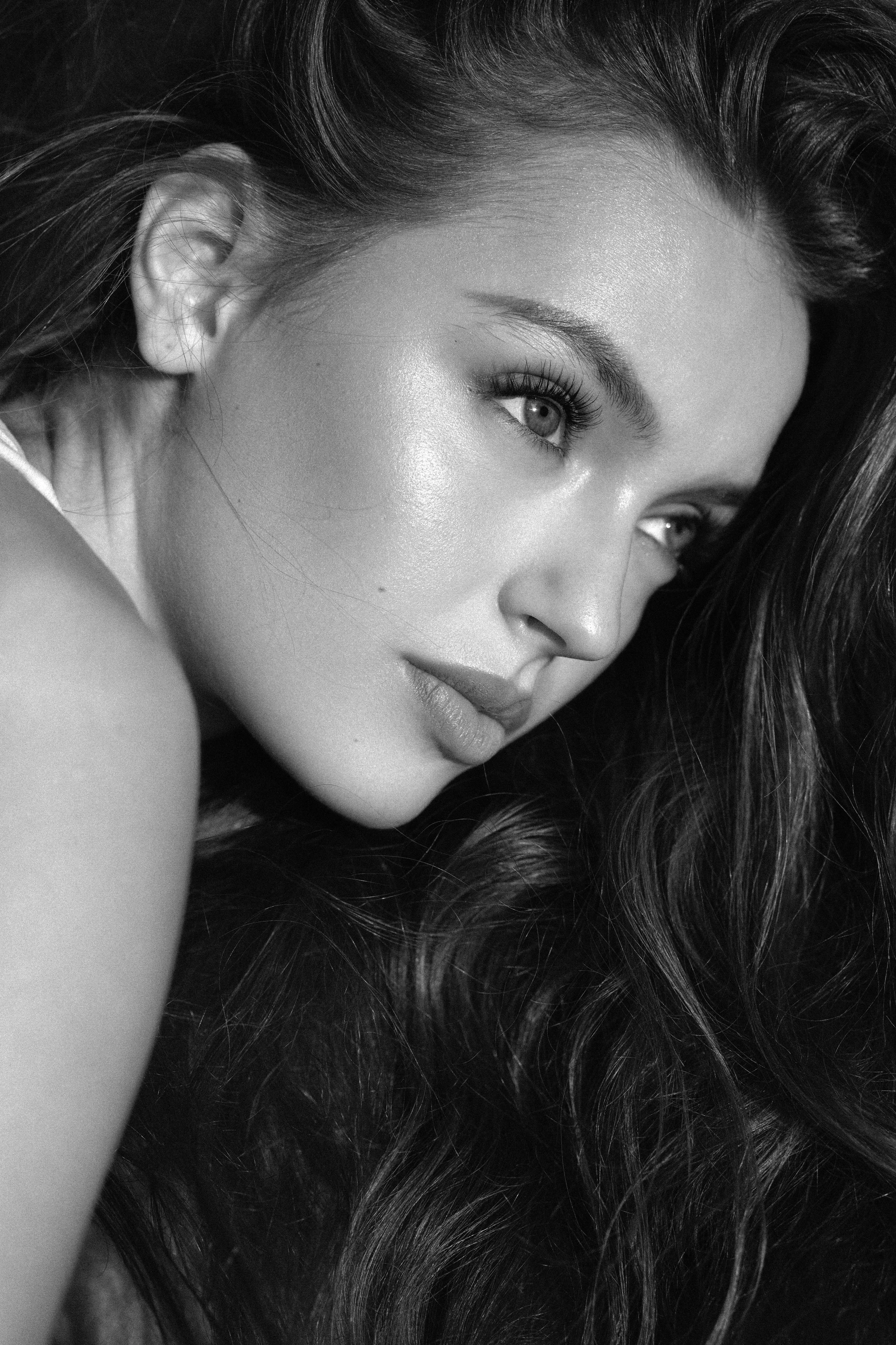 Close-up black and white portrait of a woman with long, wavy hair, gazing thoughtfully to the side.