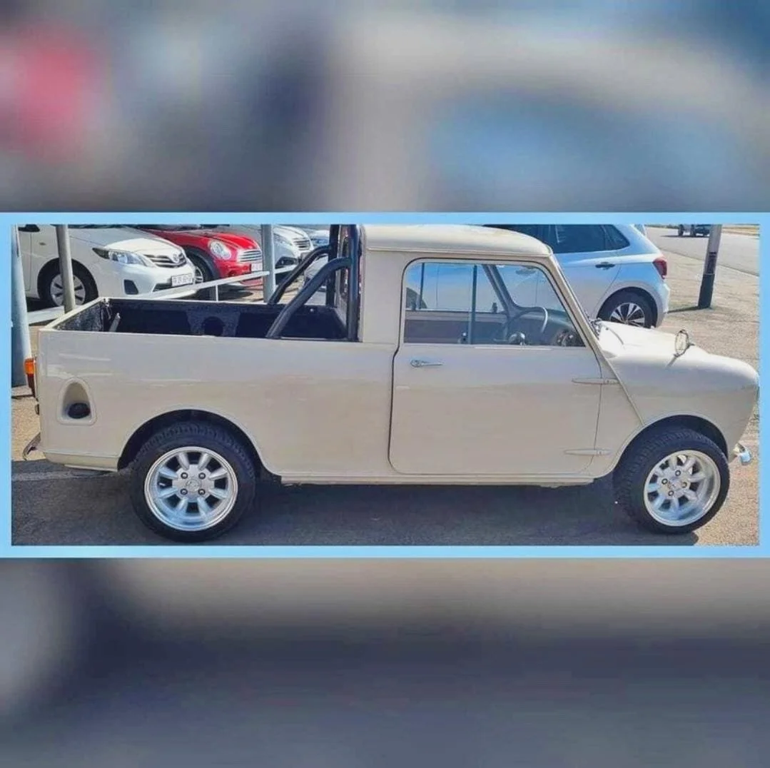 A small vintage white pickup truck parked on the street with other cars in the background.