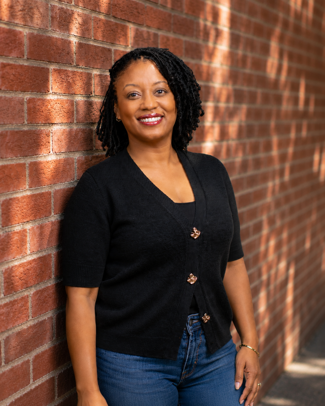 Dr. Carla smiling outdoors on a city sidewalk, wearing a black cardigan and jeans.