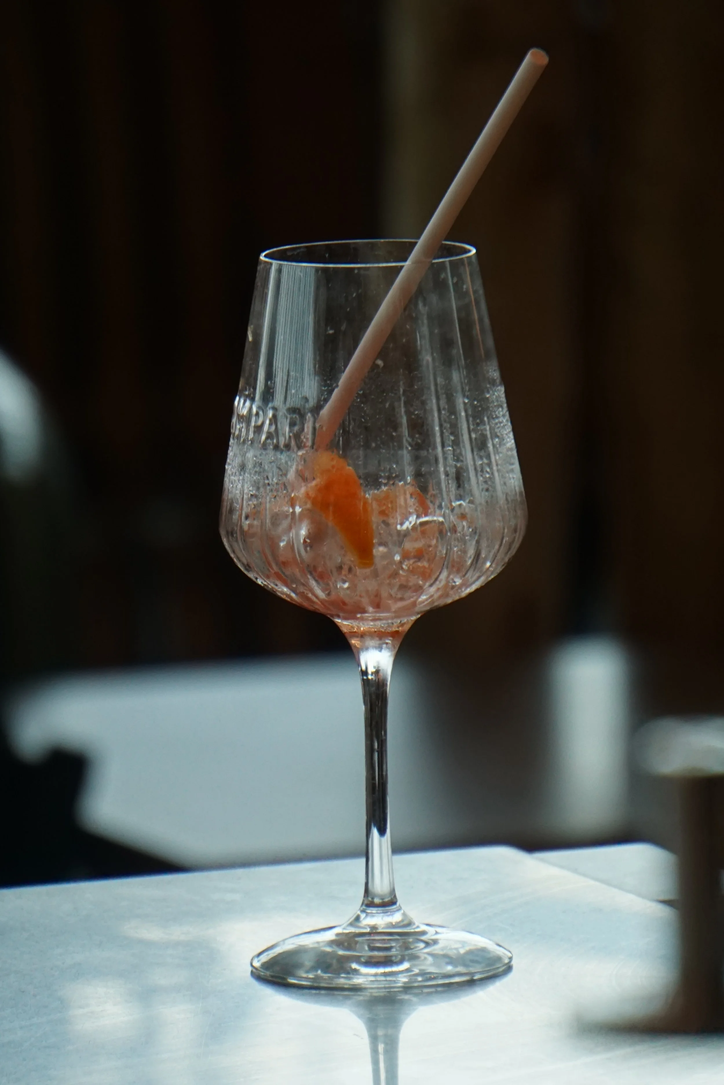 Empty cocktail glass with a slice of orange and a straw inside, resting on a white surface with a blurred dark background.