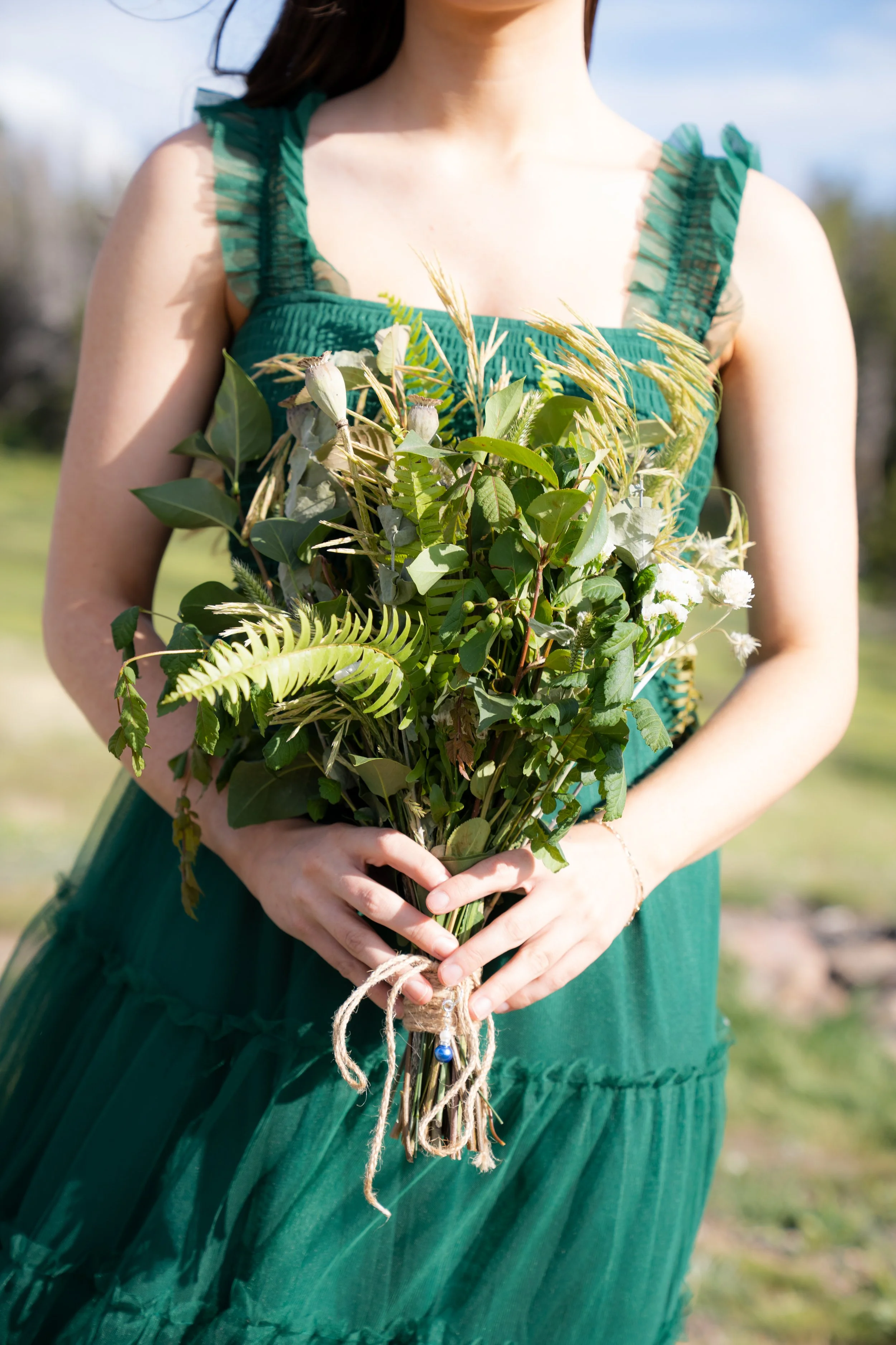 A woman in a green dress holding a bouquet of wildflowers, with a blurred outdoor background.