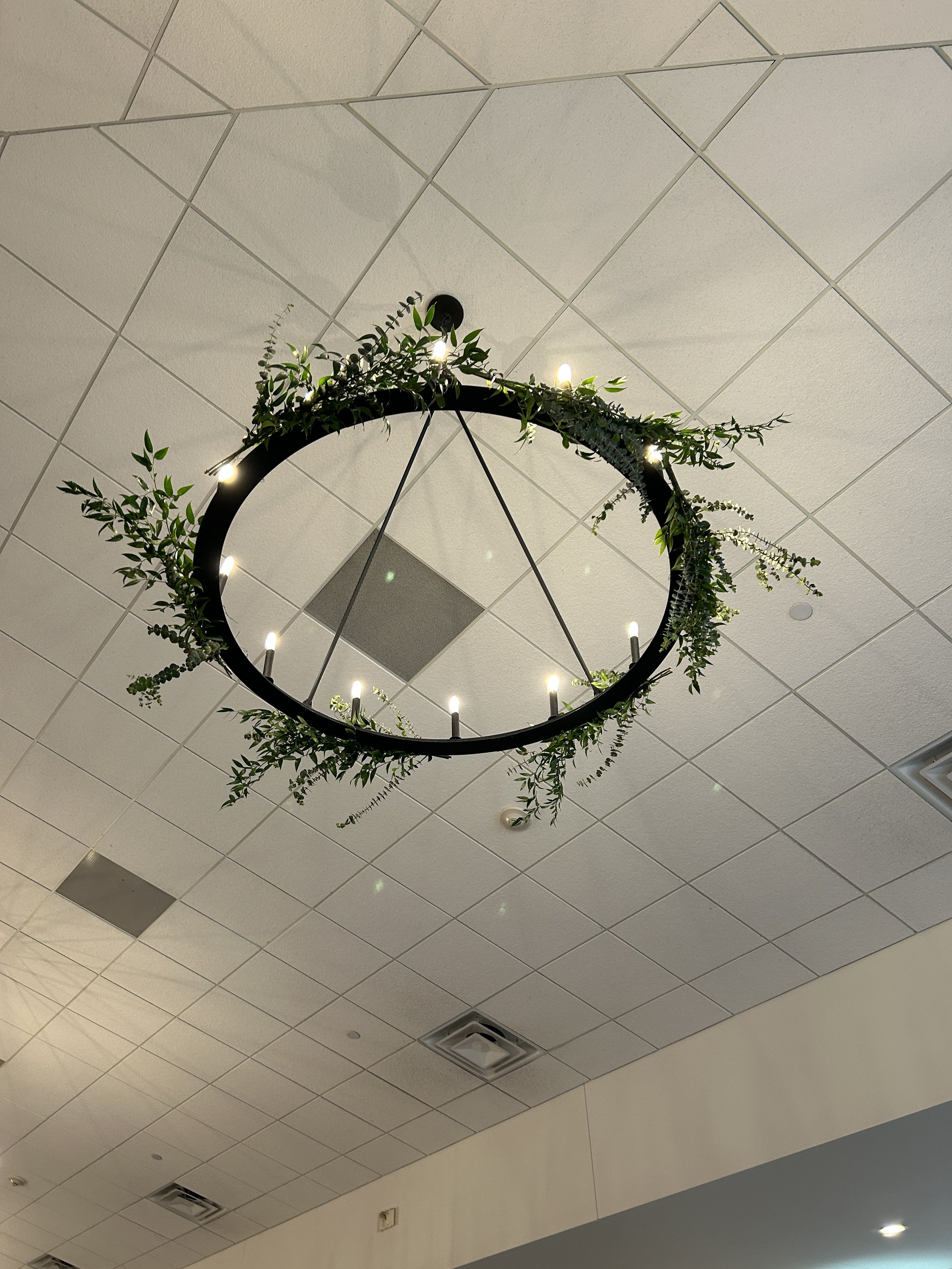 Ceiling with a modern circular chandelier decorated with green foliage and small white lights.