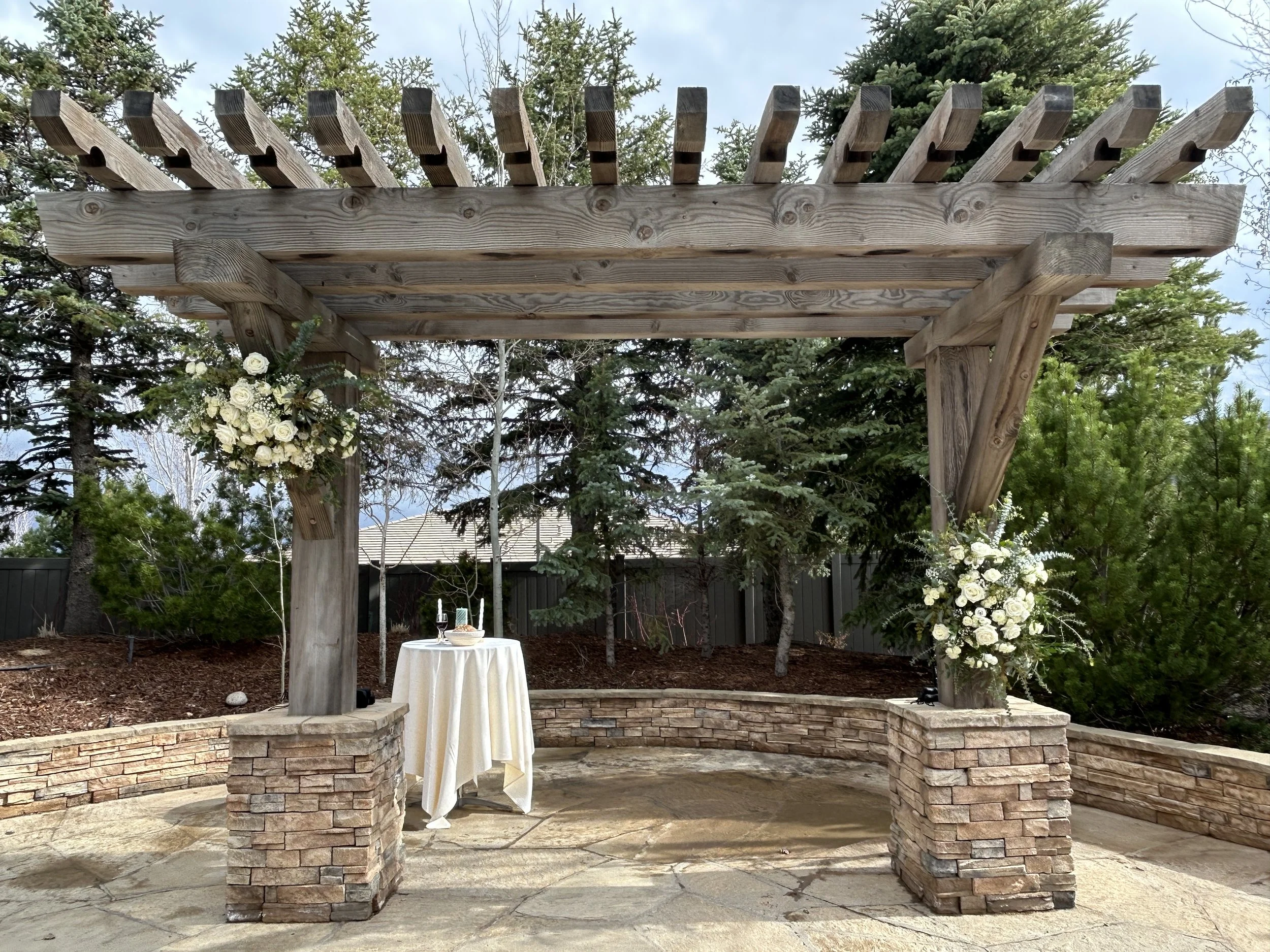 Decorative outdoor pergola structure with flowers and a small round table underneath.