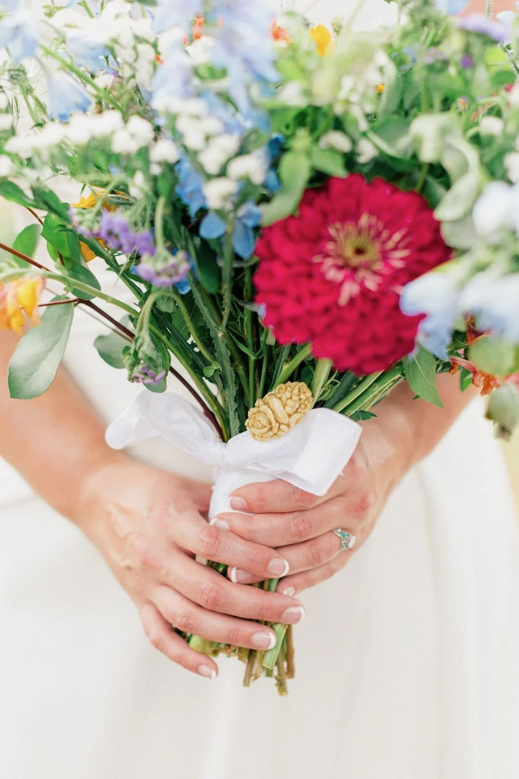 Person holding a bouquet of mixed colorful flowers wrapped with white cloth.