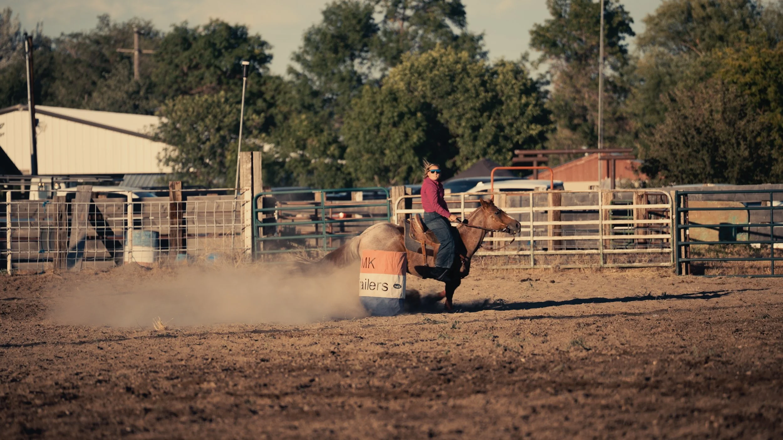 A person riding a horse around a barrel in a dirt arena during a rodeo or equestrian event.