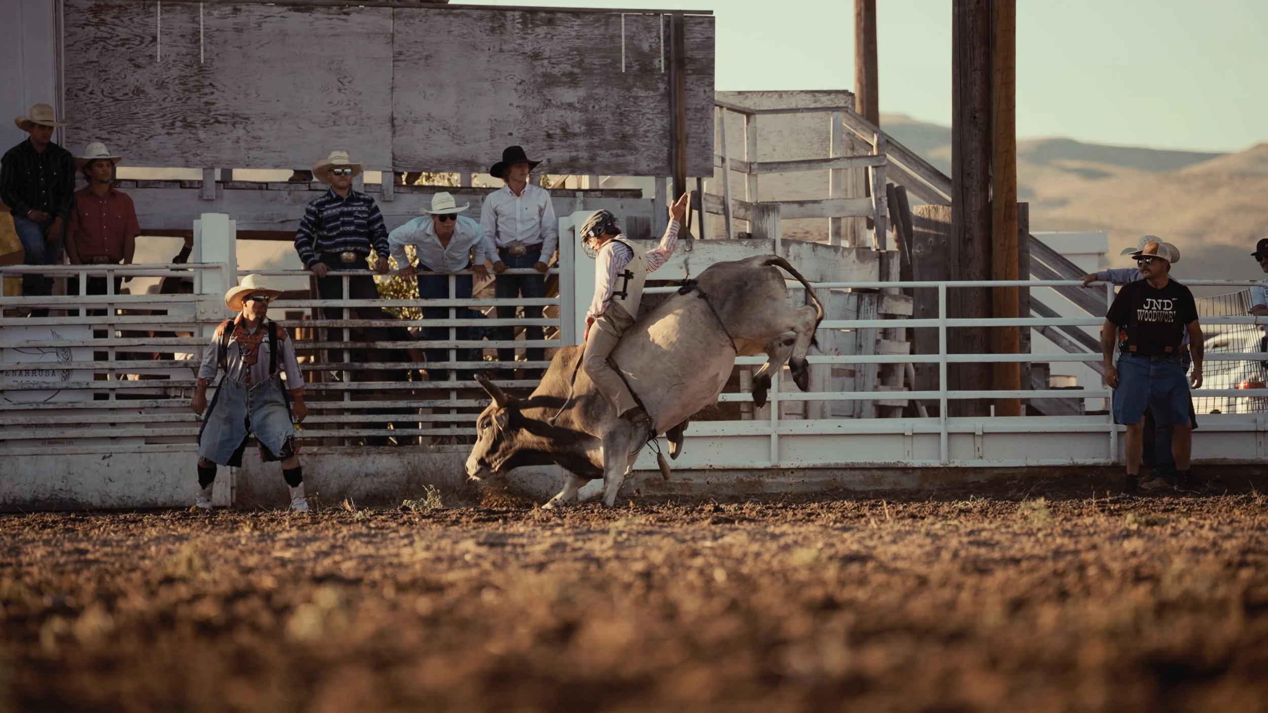 Cowboy riding a bull during a rodeo, with several spectators watching from behind the fence.