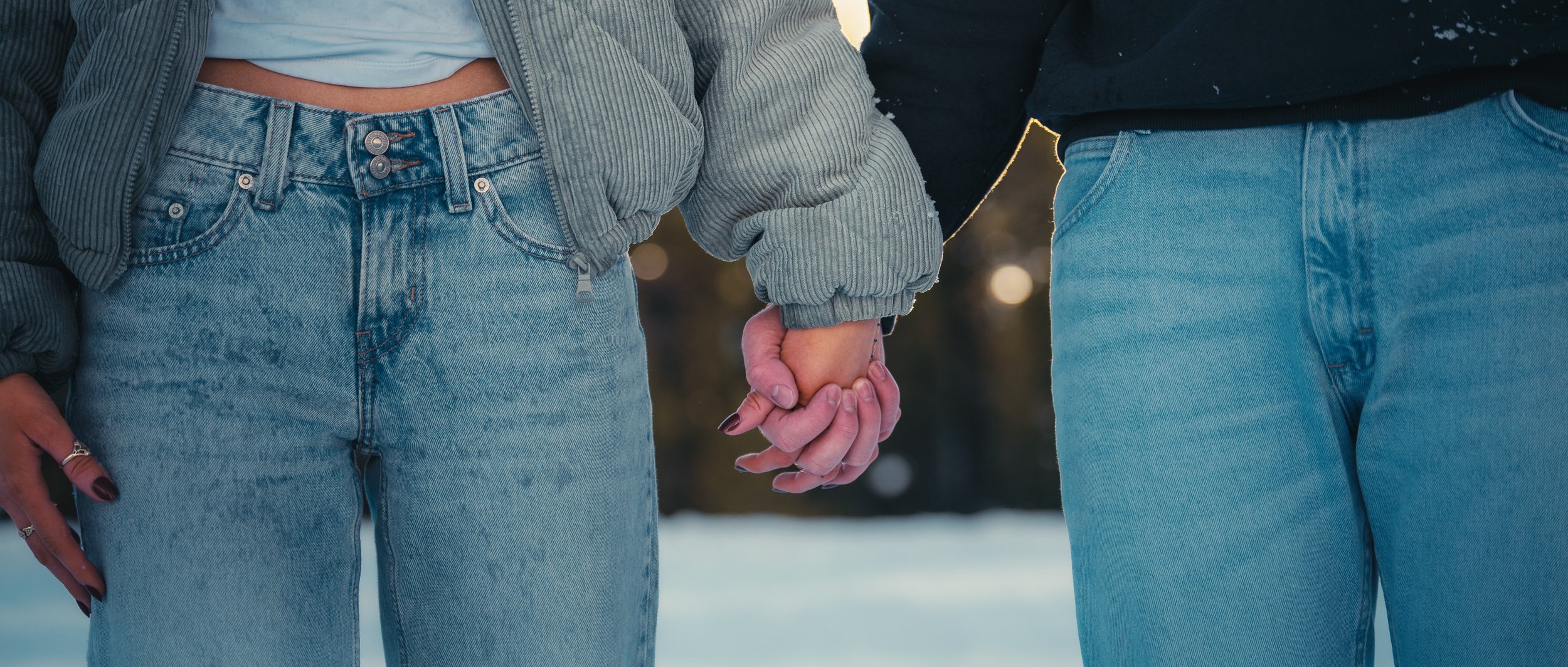 A couple holding hands outdoors in winter, wearing blue jeans and jackets.