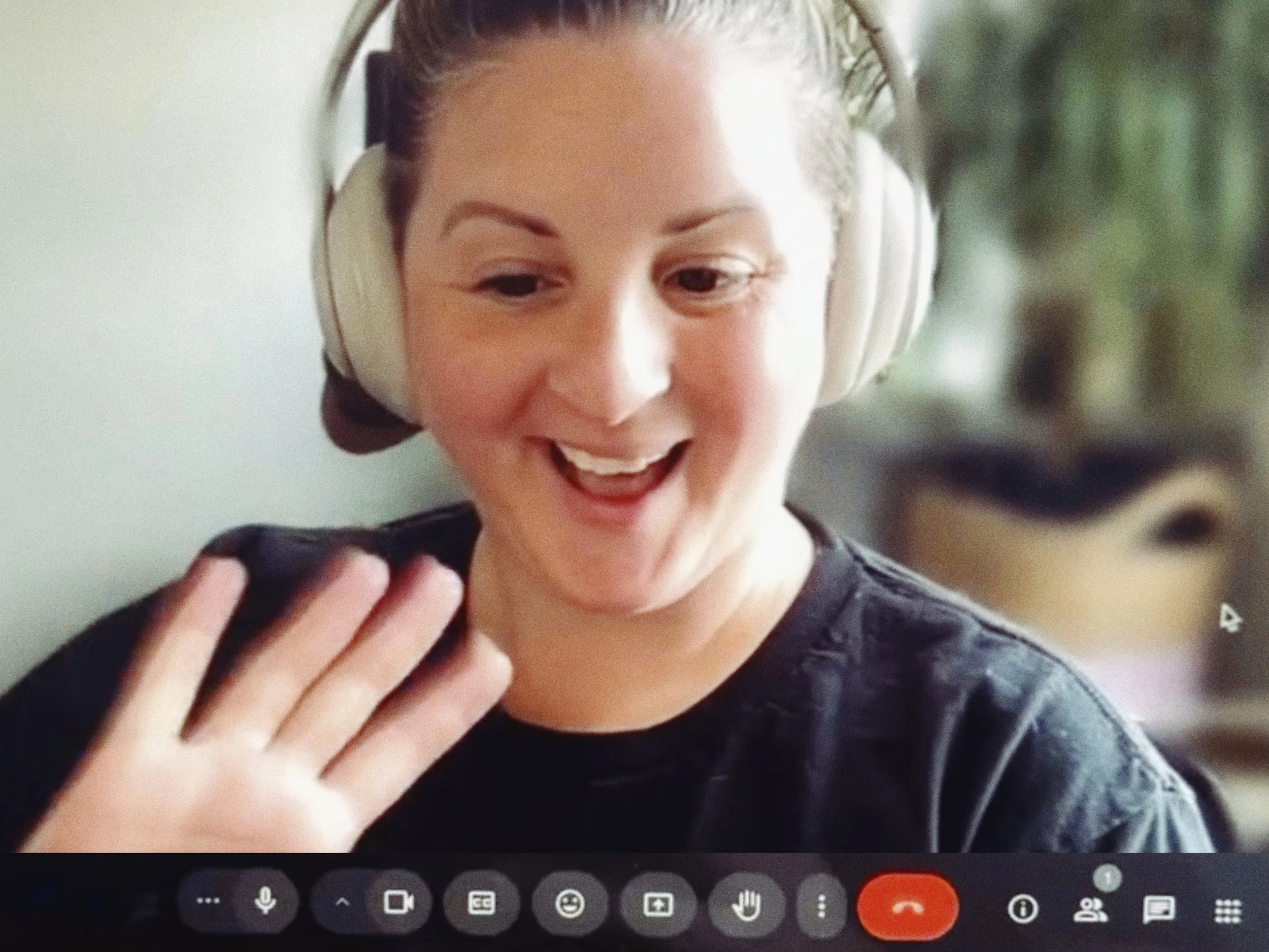 A white woman waves at the camera looking slightly downward and at the bottom of the screen are icons indicating that she is on a video chat.