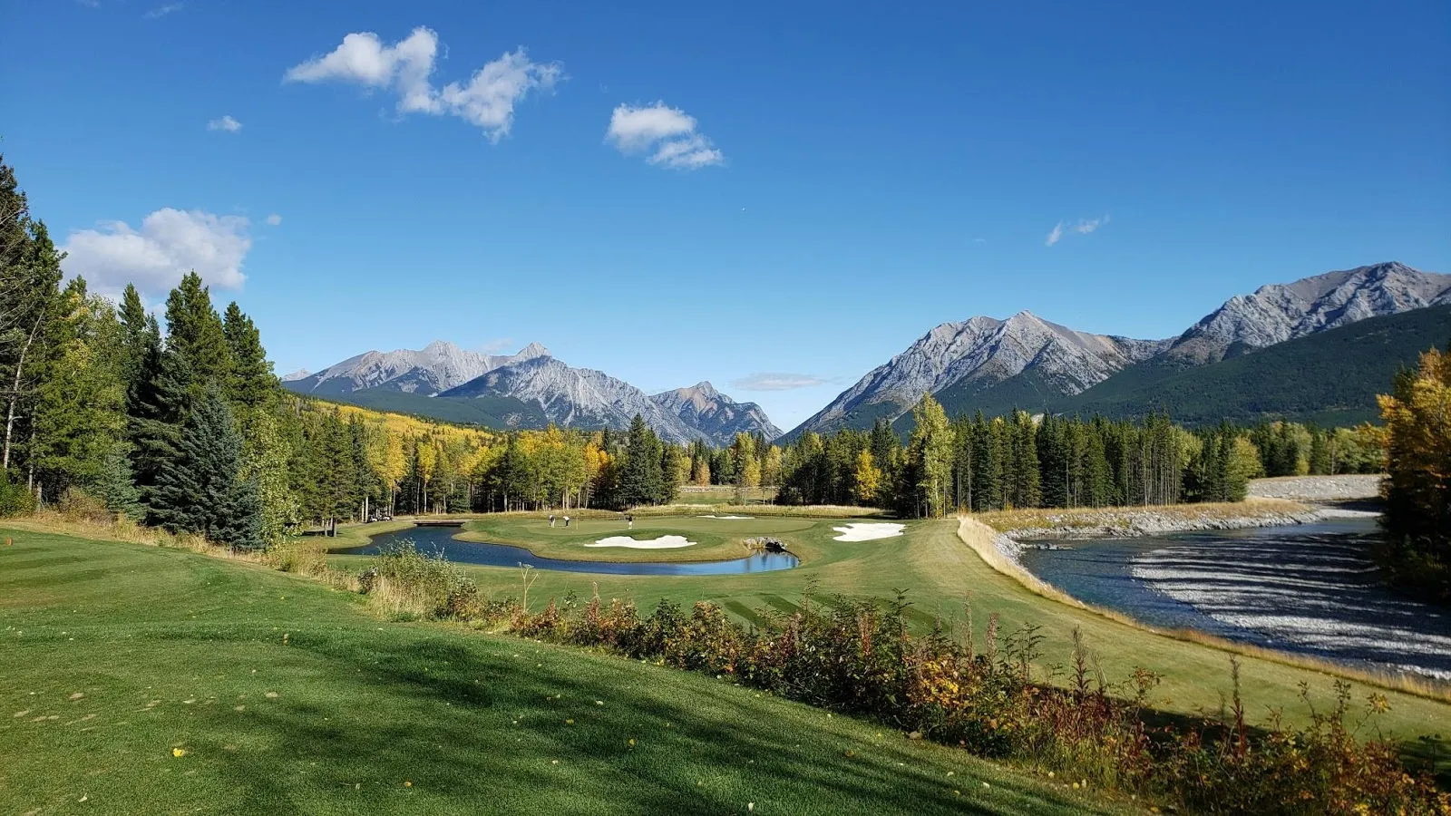 Scenic golf course with mountains and trees in the background under a clear blue sky.